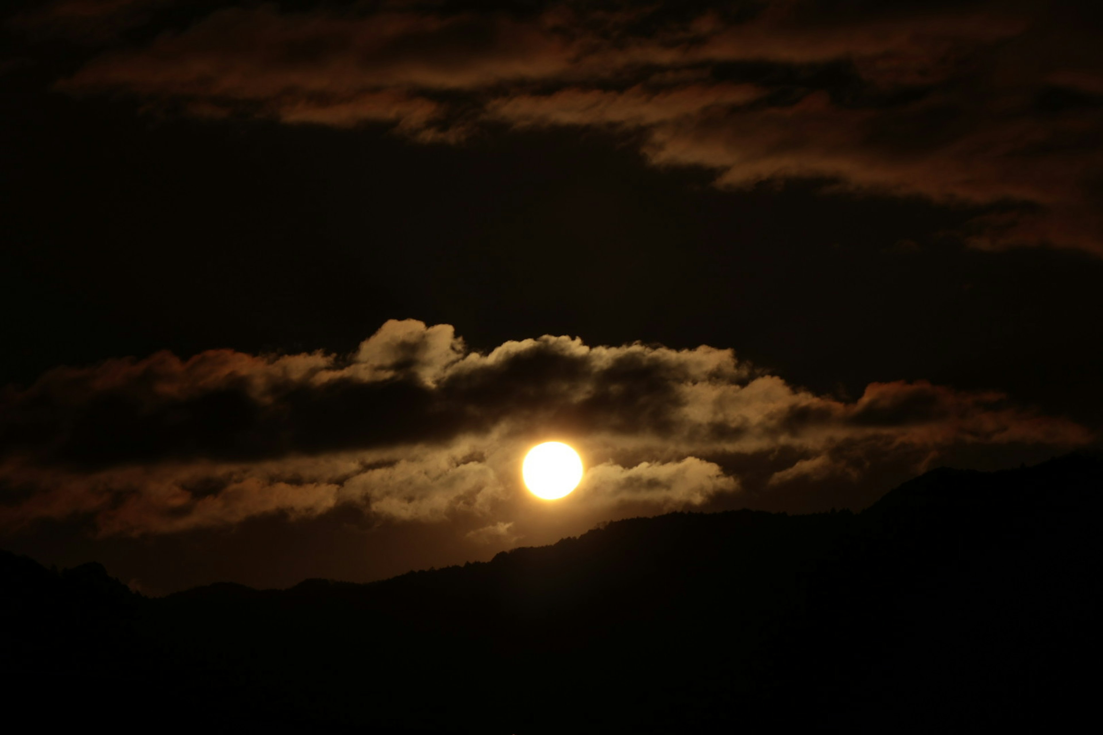 Silhouette des Sonnenuntergangs, der durch die Wolken blitzt