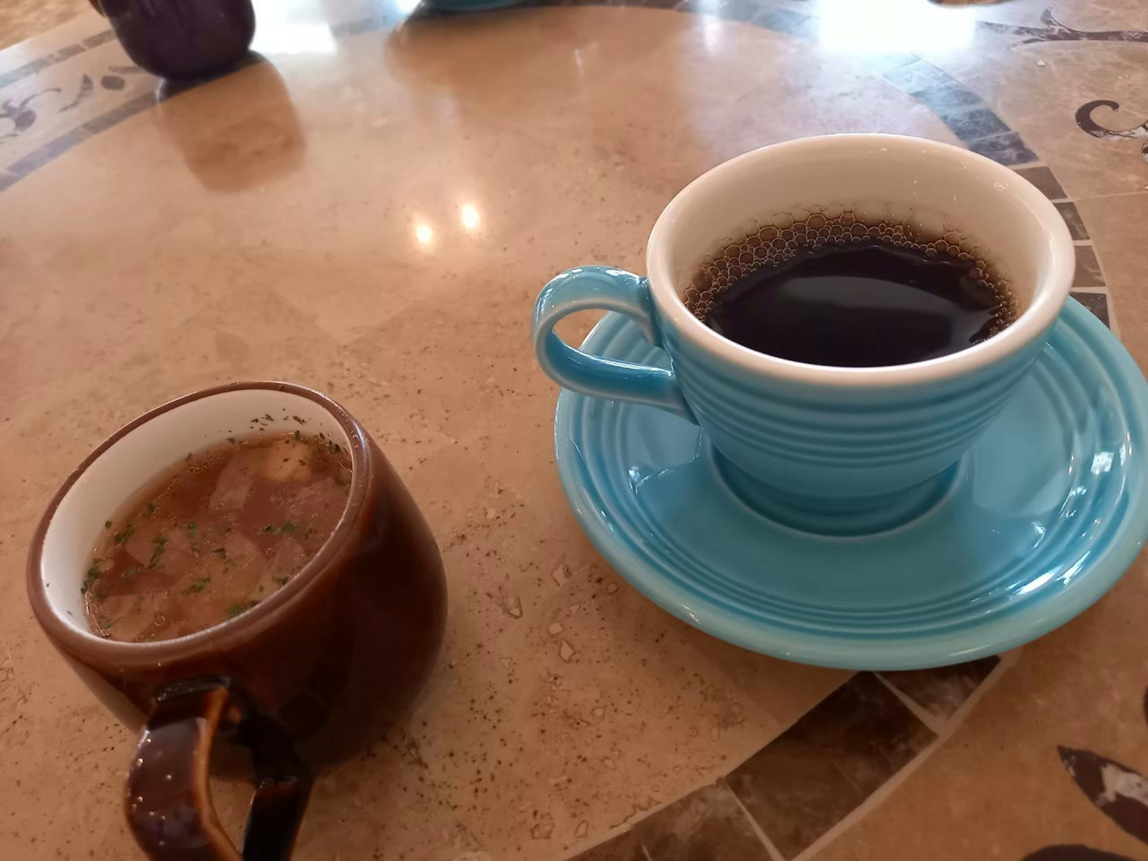 Ein Foto von zwei Kaffeetassen auf einem Tisch mit einer braunen Tasse, die hellen Kaffee links enthält, und einer blauen Tasse mit schwarzem Kaffee rechts