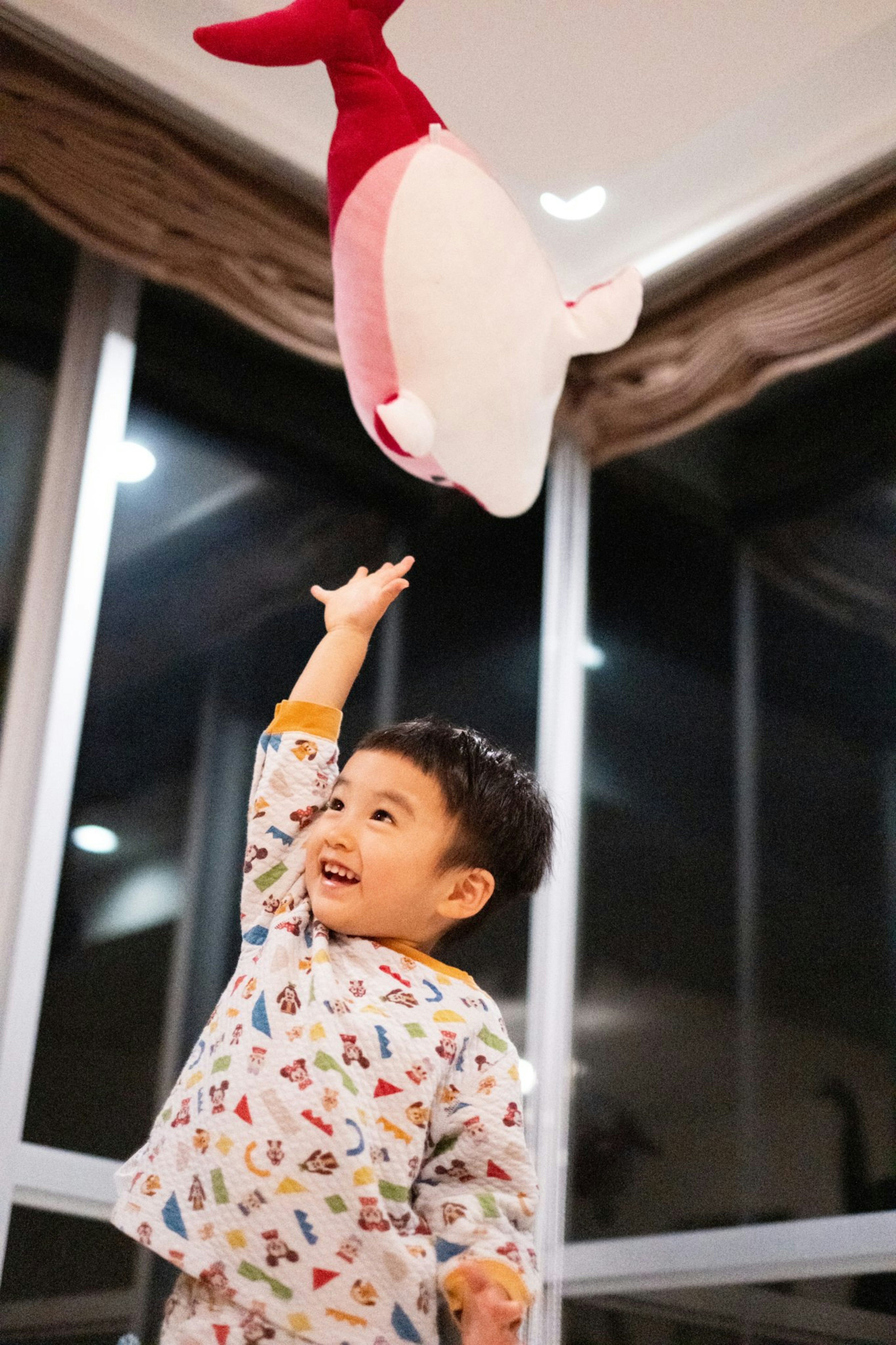 Un niño alcanzando un pez de peluche rojo y blanco en un entorno acogedor