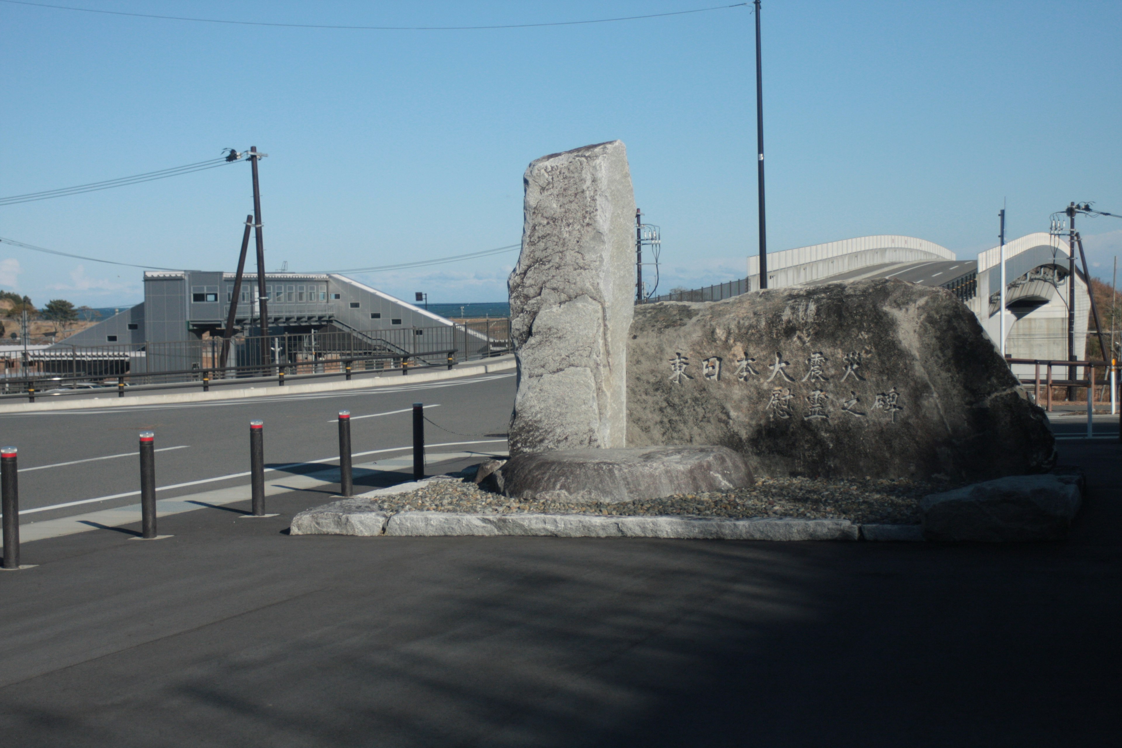 Large rock and concrete structure by the roadside with buildings in the background