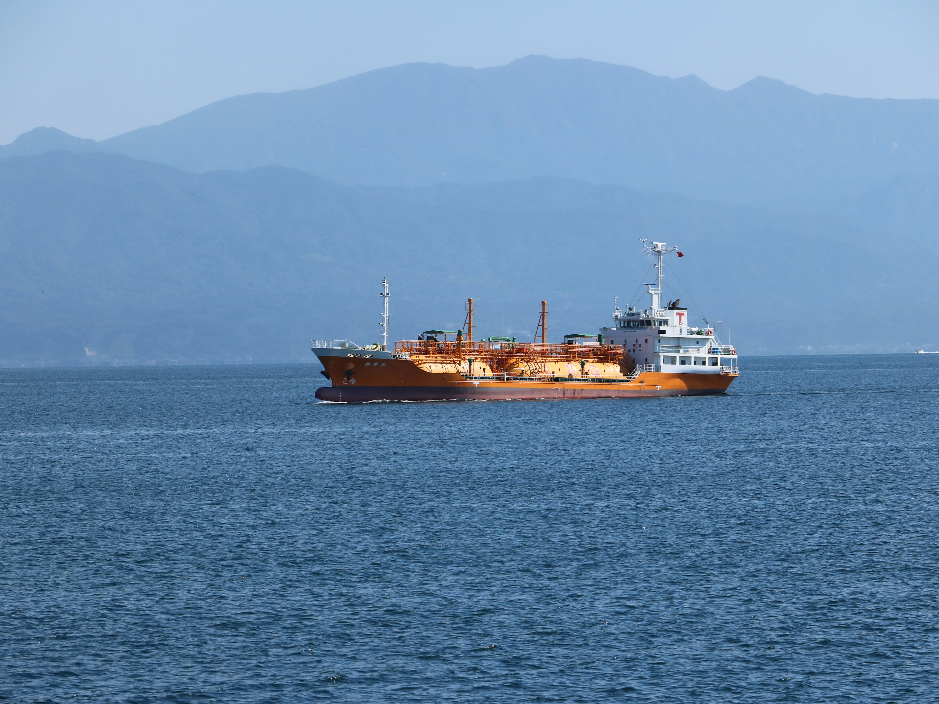 Kapal kargo yang berlayar di laut dengan warna-warna cerah dan latar belakang pegunungan