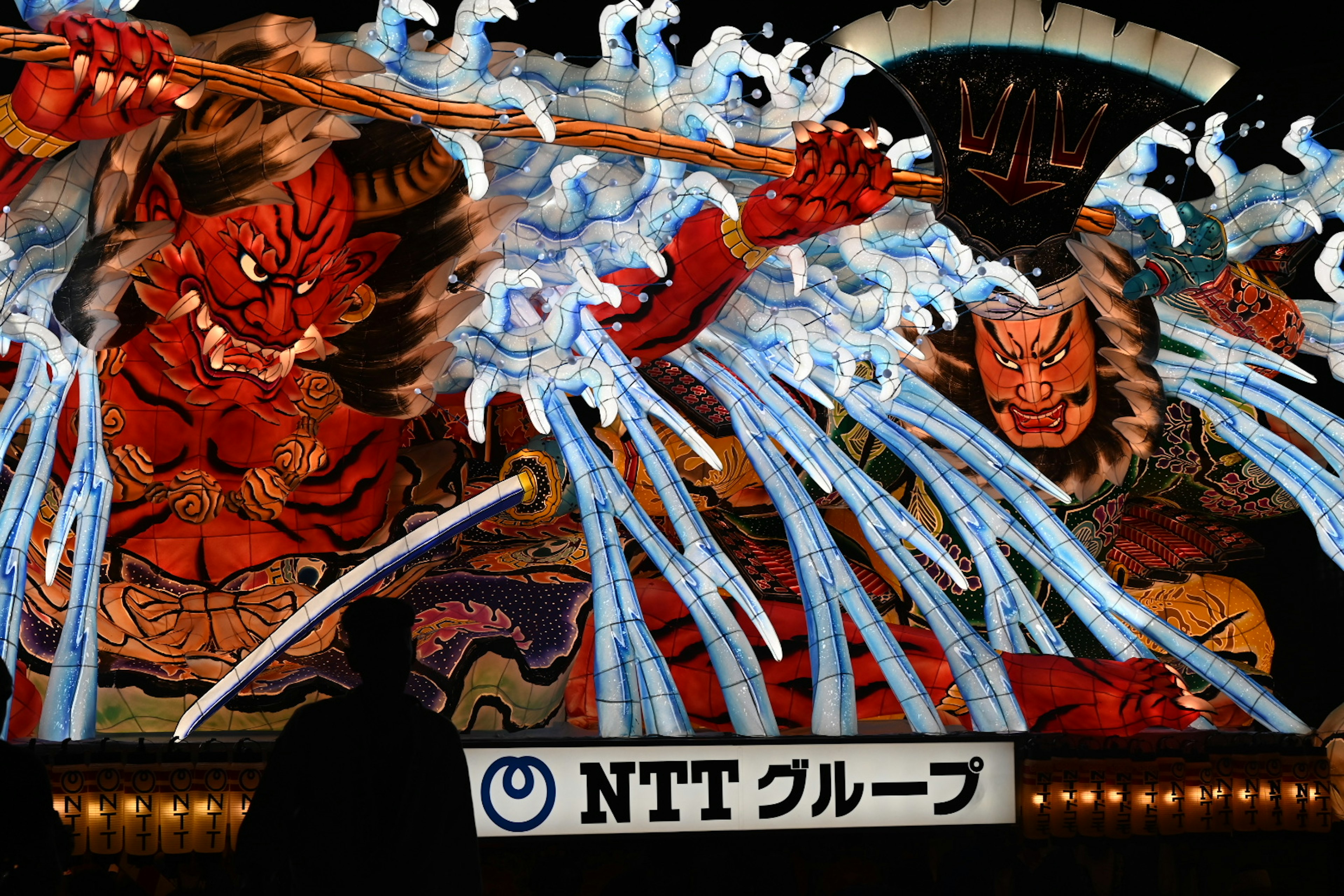 Large festival decoration featuring demons splashing water and NTT Group logo