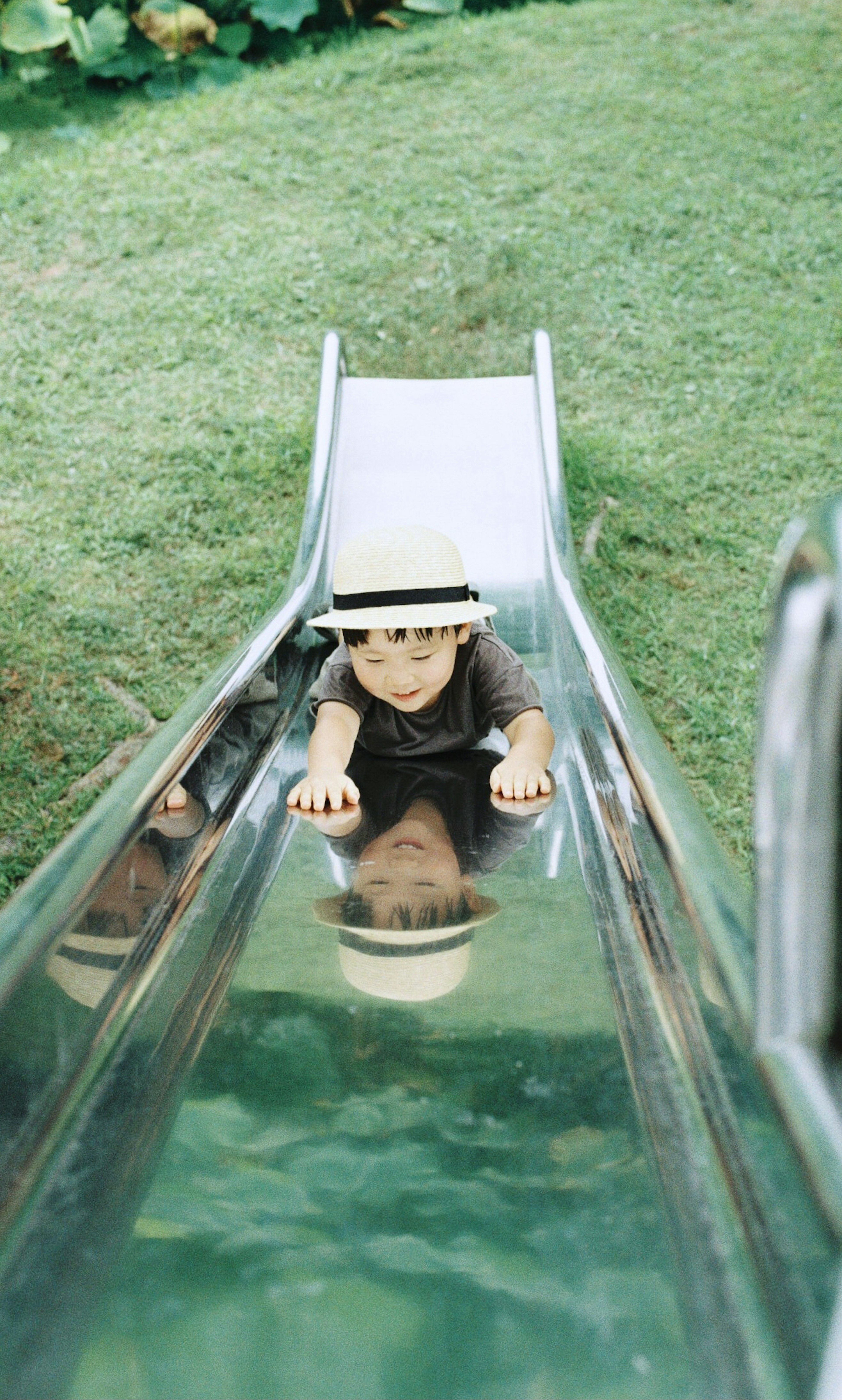 A child climbing a slide wearing a hat on green grass