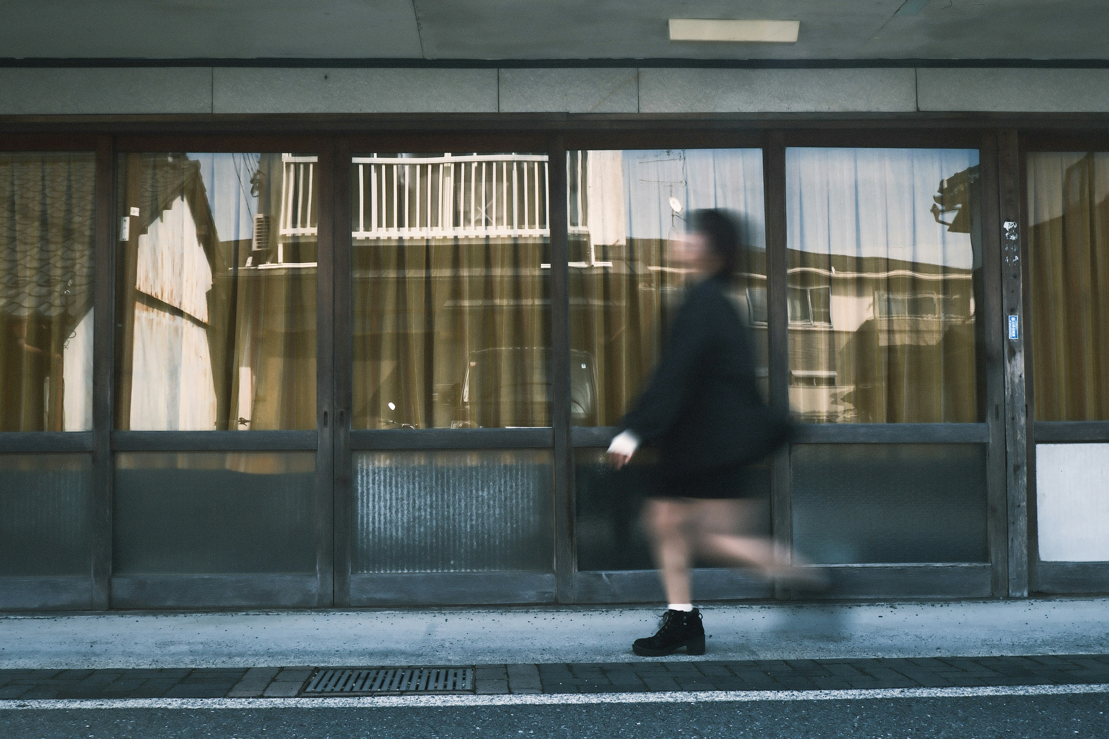一位女性走过一座现代建筑，建筑有大窗户和窗帘