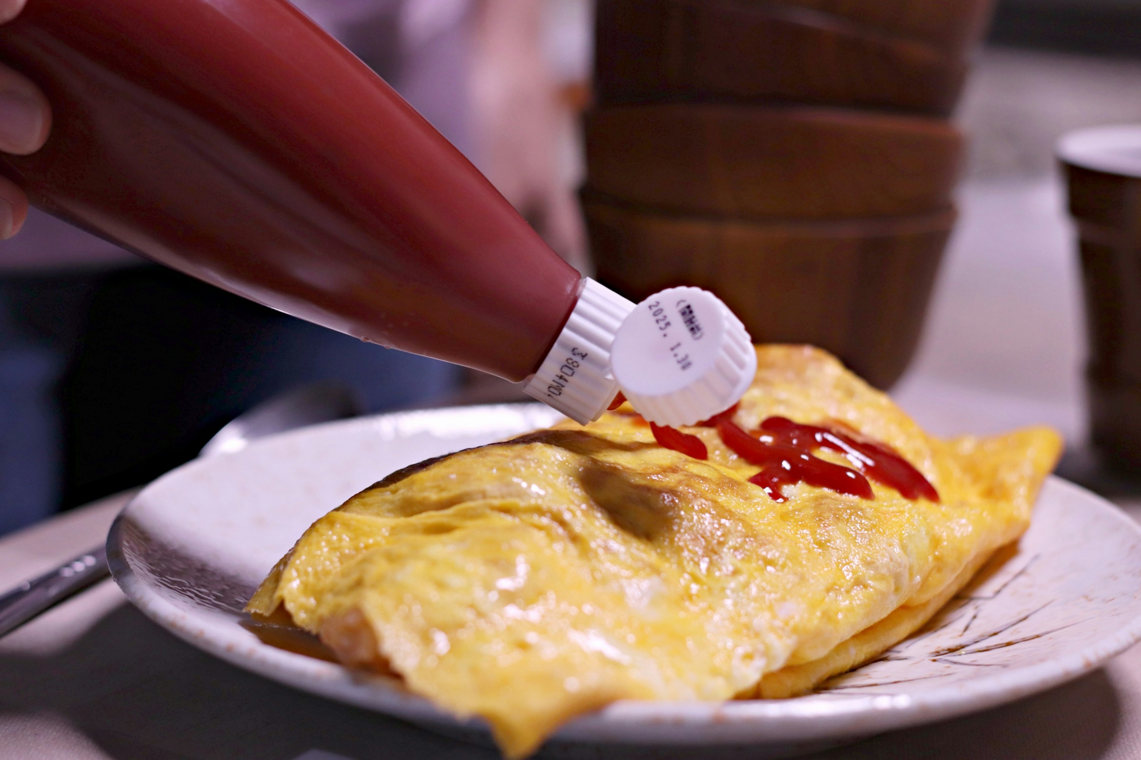 A plate of omelette being topped with ketchup