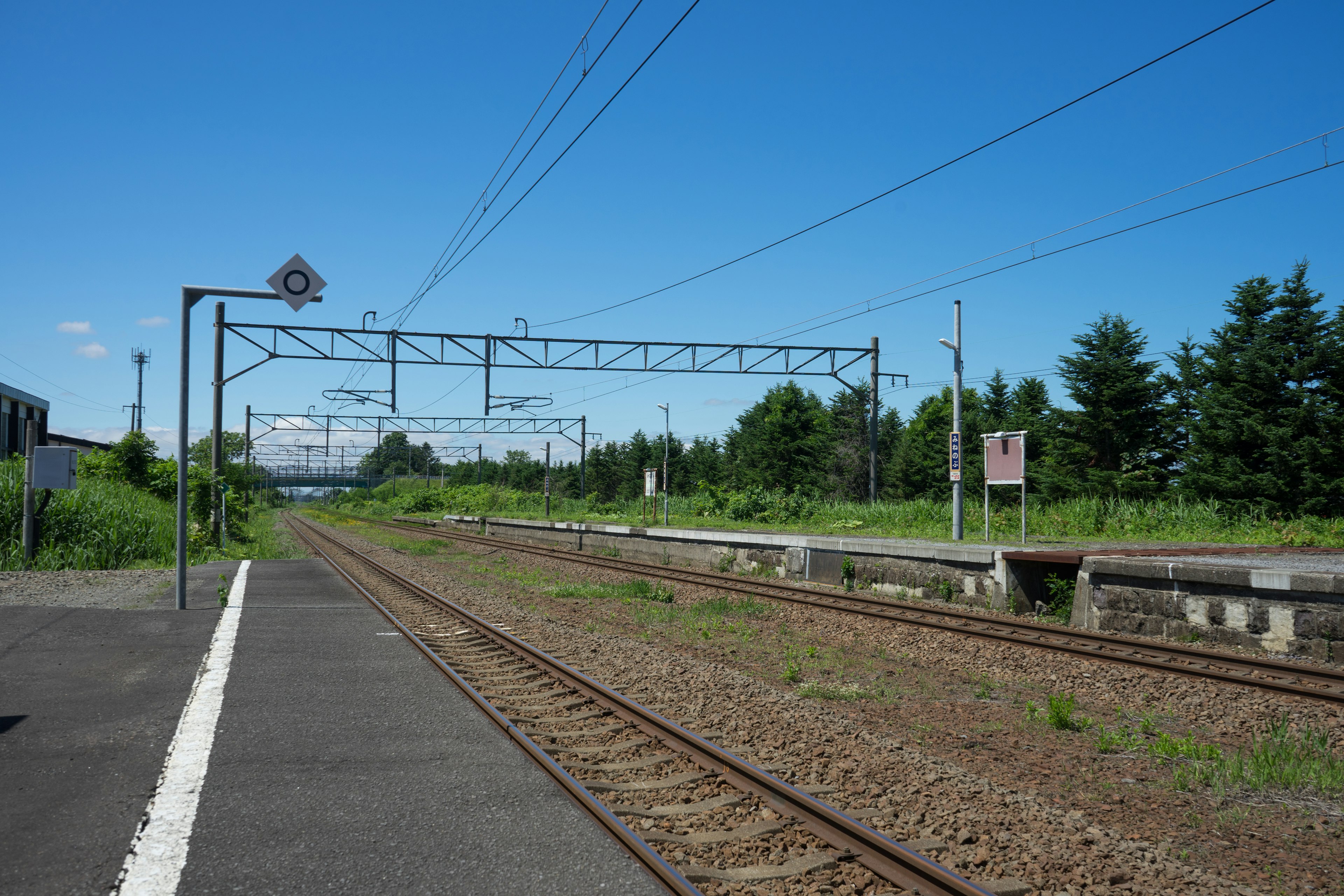 Escena de estación de tren bajo un cielo azul con vías y plataforma