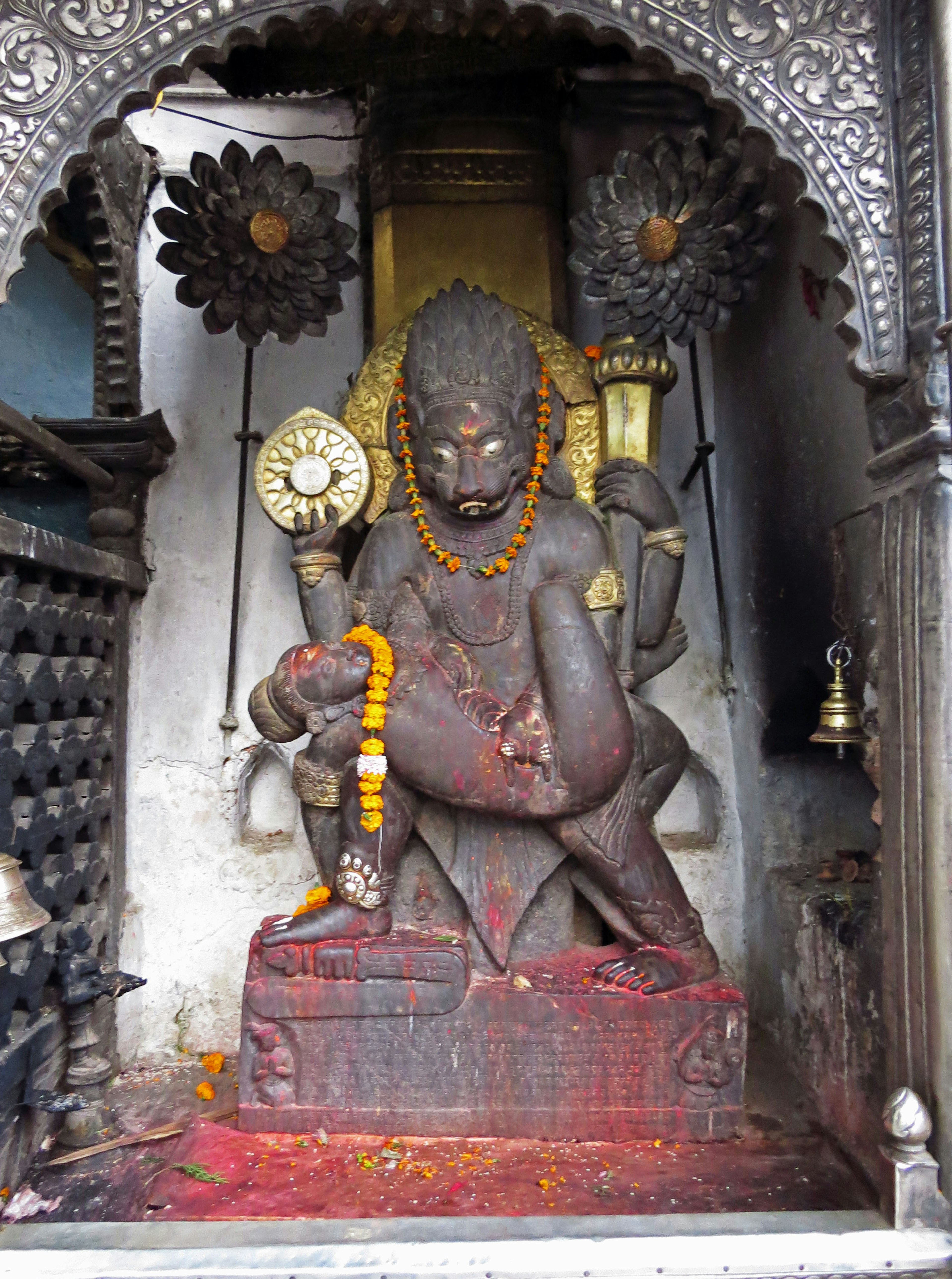 Hindu deity statue in a temple with a decorated background and garland