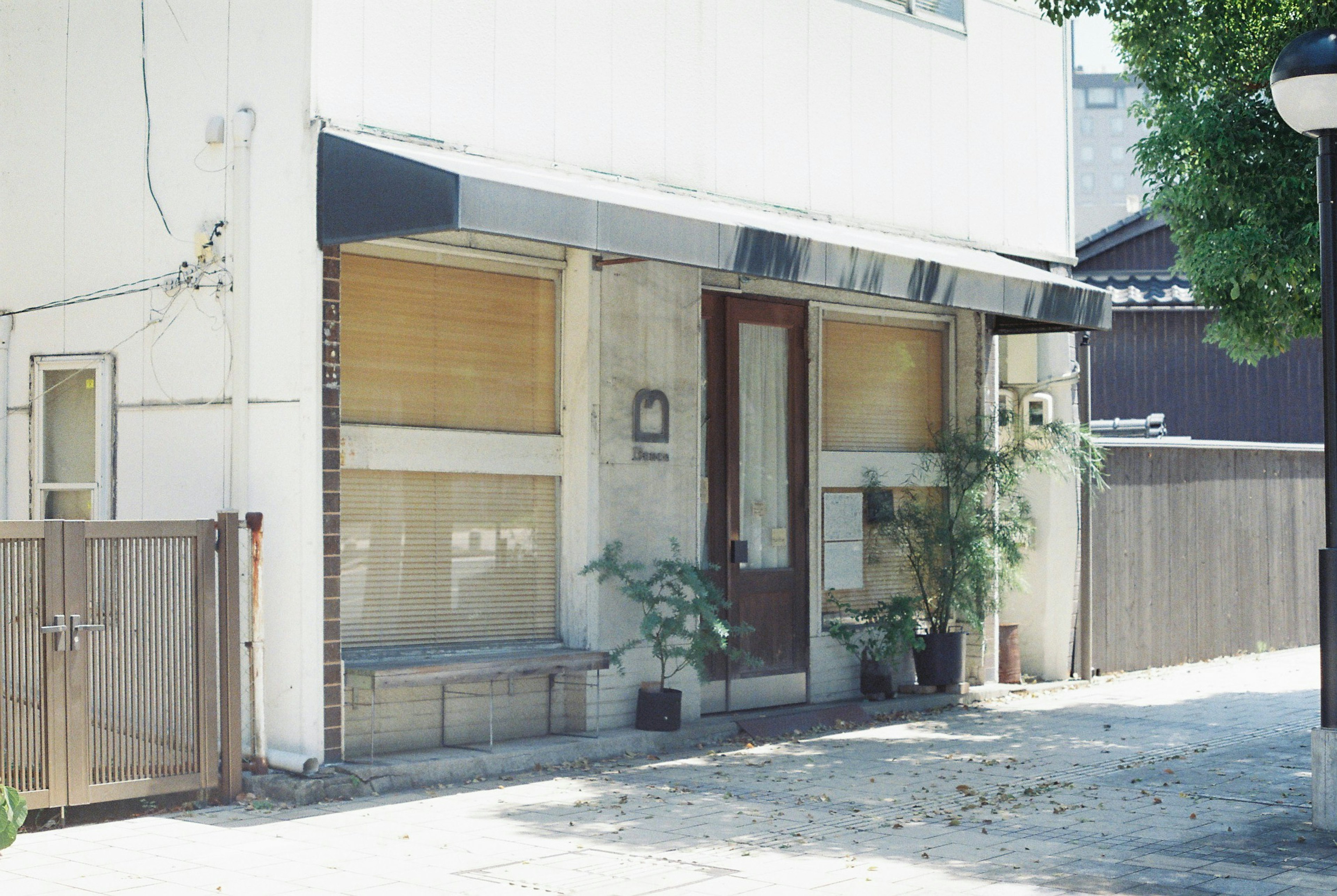 Entrée d'un bâtiment avec des murs blancs et un auvent noir présentant des plantes en pot et une porte en bois