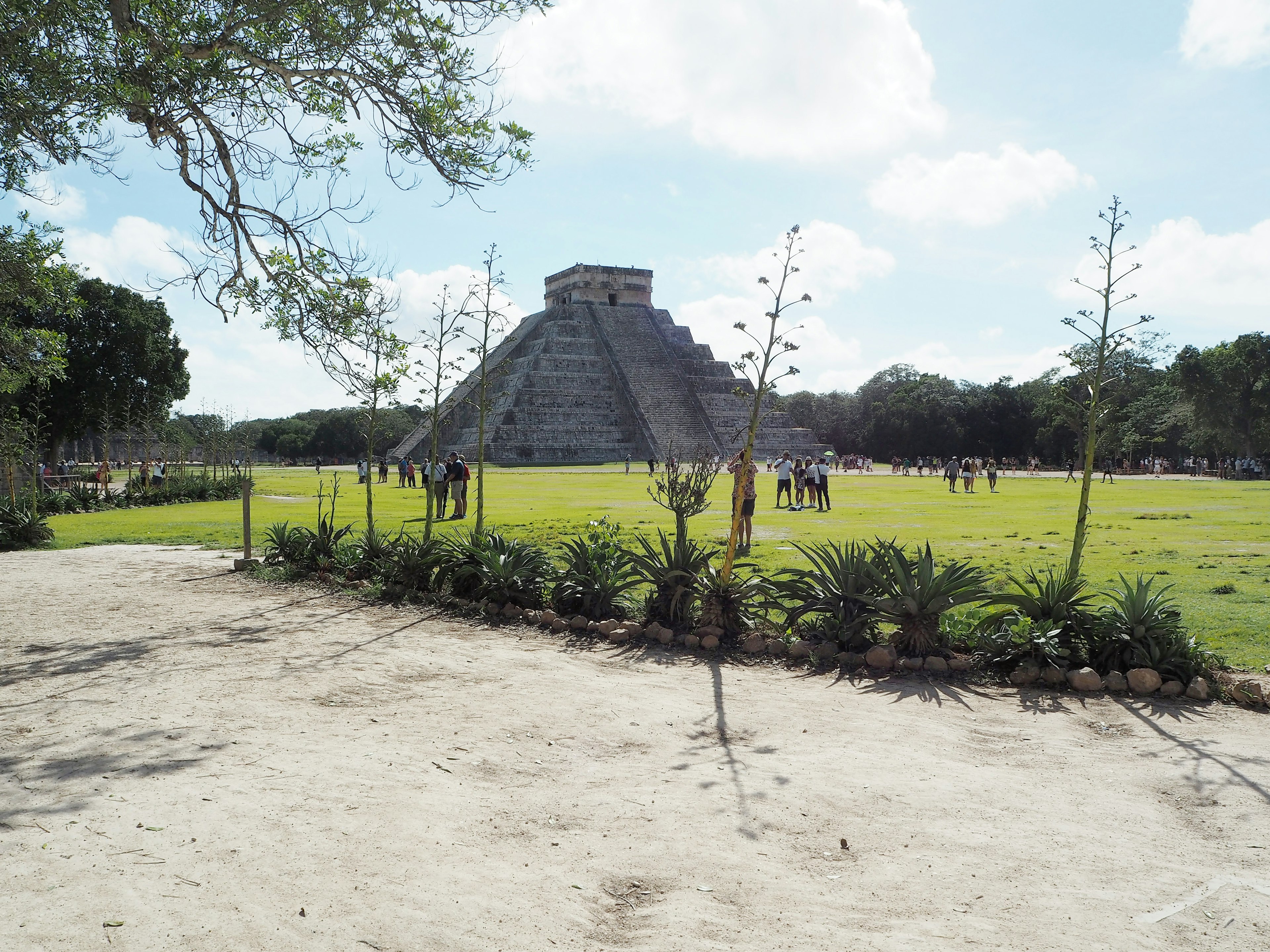 Vista della piramide di Chichen Itza con vegetazione circostante e visitatori