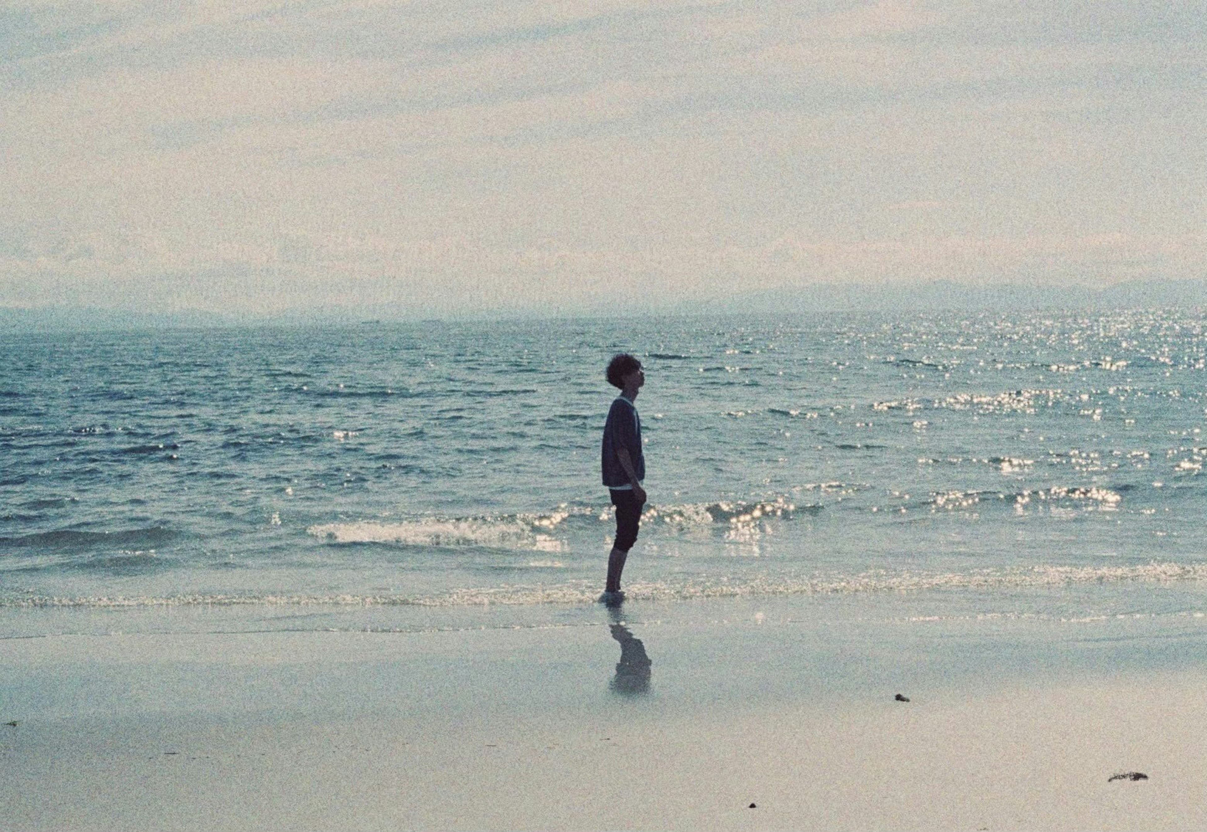 Un niño de pie en la playa mirando al océano con colores suaves del cielo