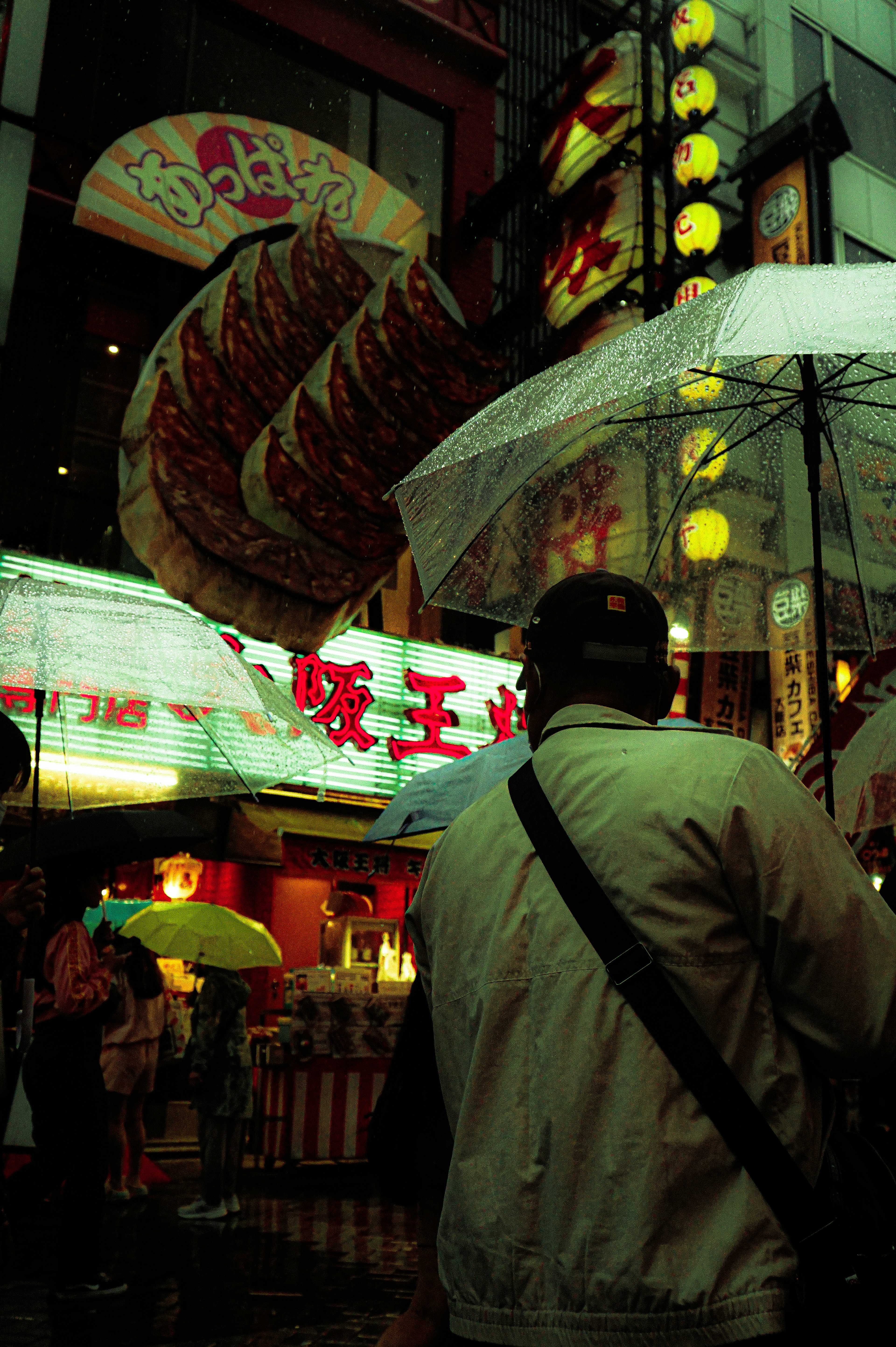 雨の中で傘を持っている人と明るい看板がある繁華街の風景