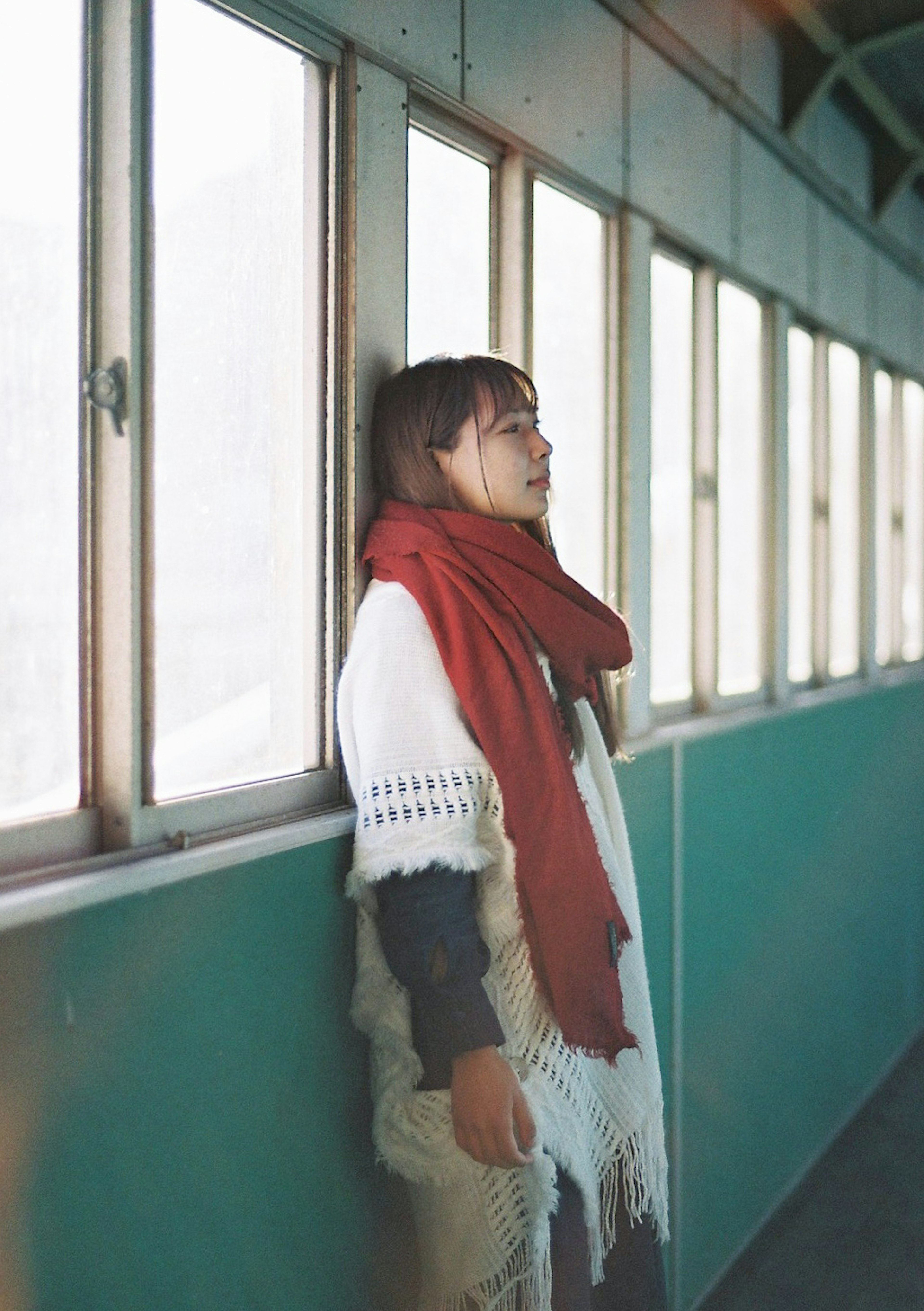 A woman standing near a window wearing a red scarf