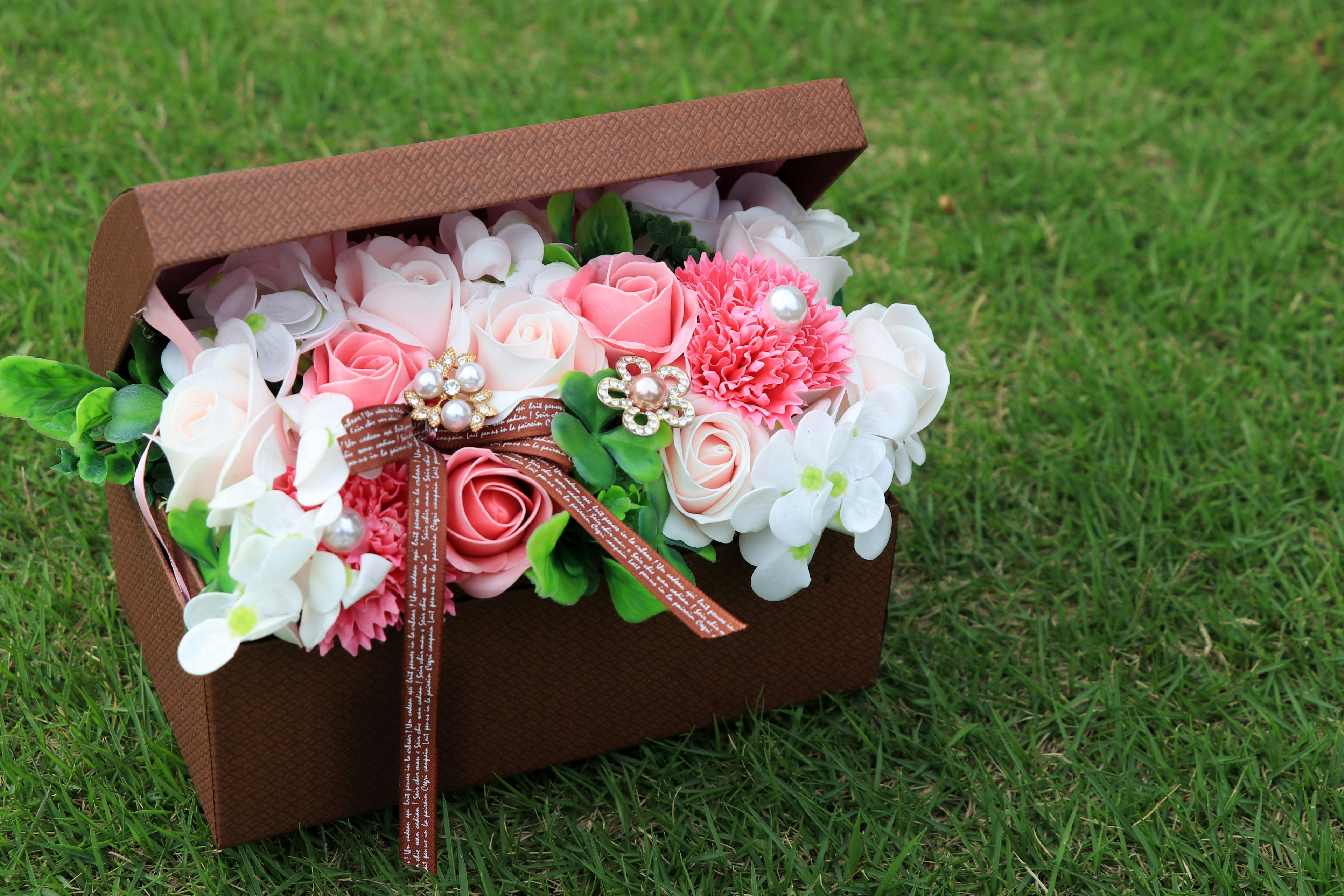 Un bouquet de fleurs roses et blanches dans une boîte marron posé sur de l'herbe verte