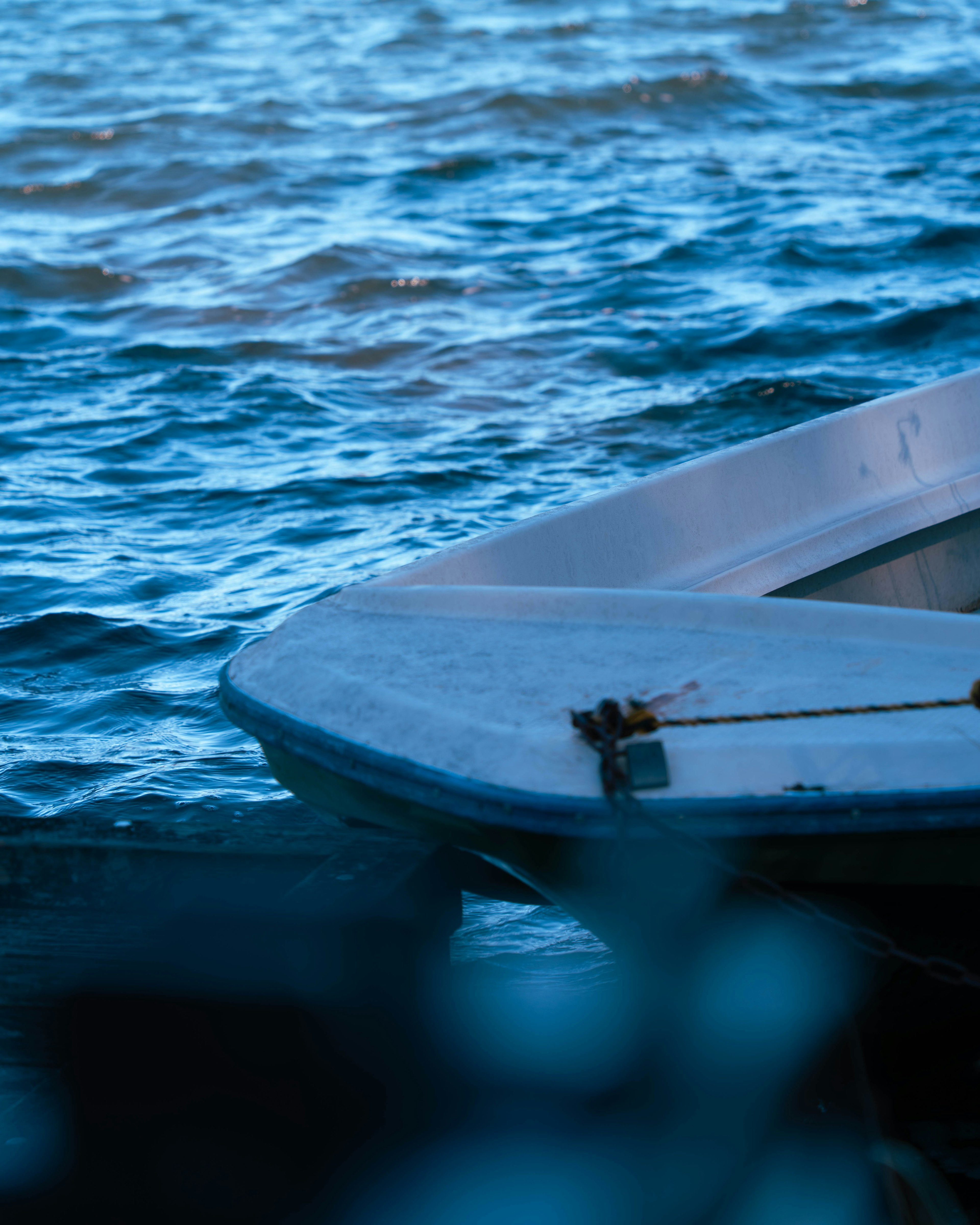 Bow of a small boat resting on blue water with a rope