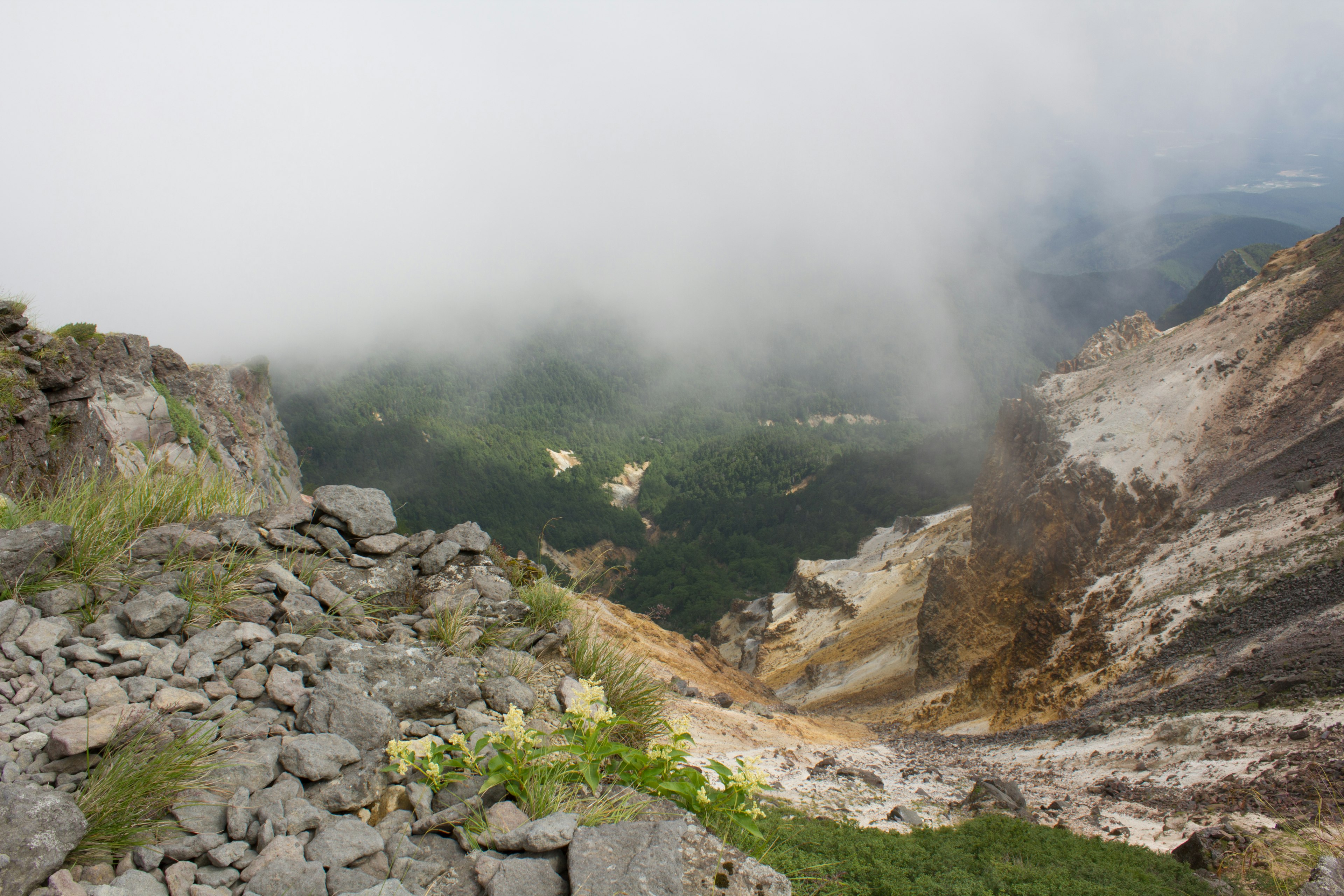 Blick von einem Berghang auf ein nebliges Tal und felsiges Gelände