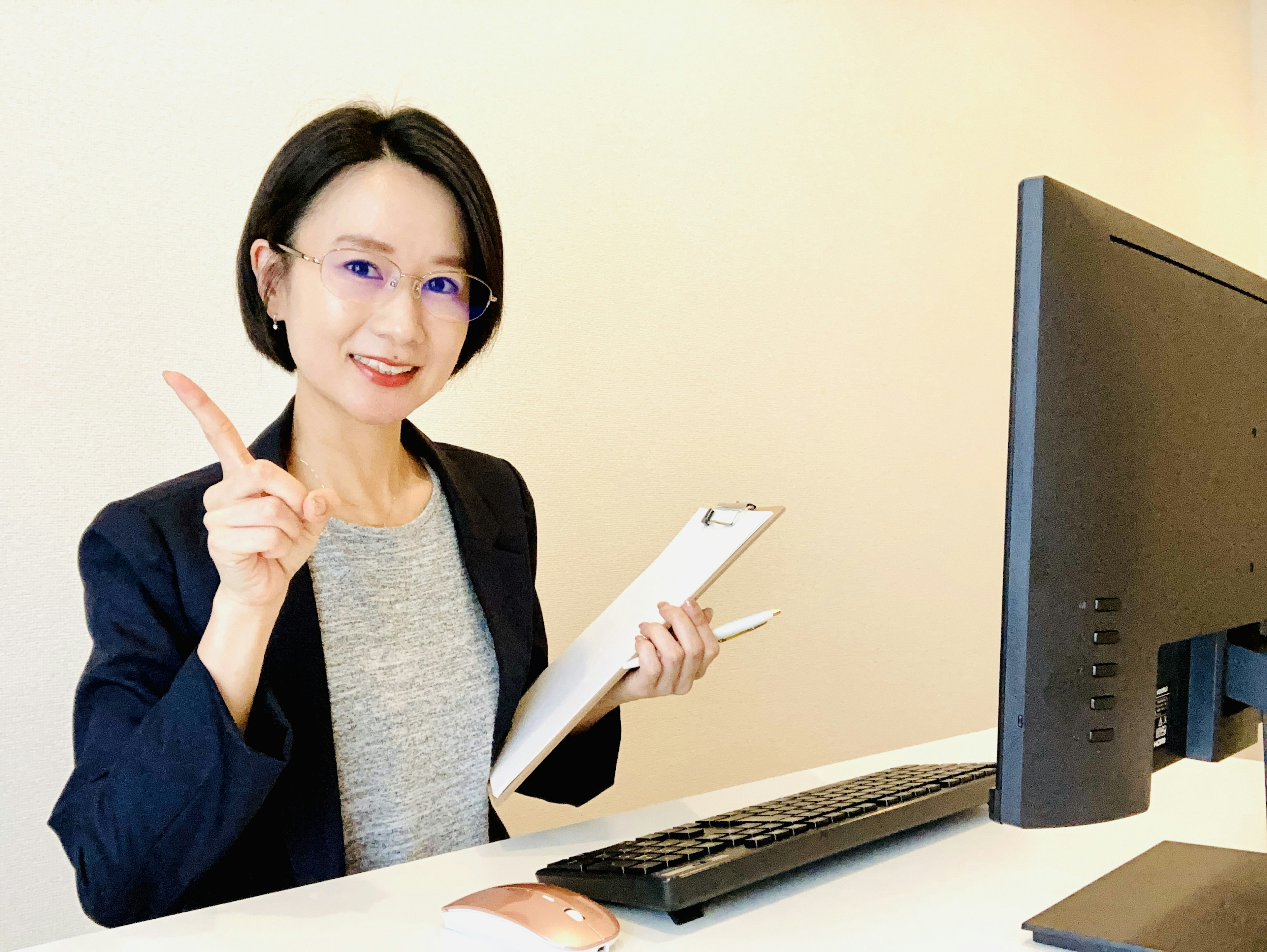 Una mujer sentada en un escritorio frente a una computadora sonriendo y levantando un dedo