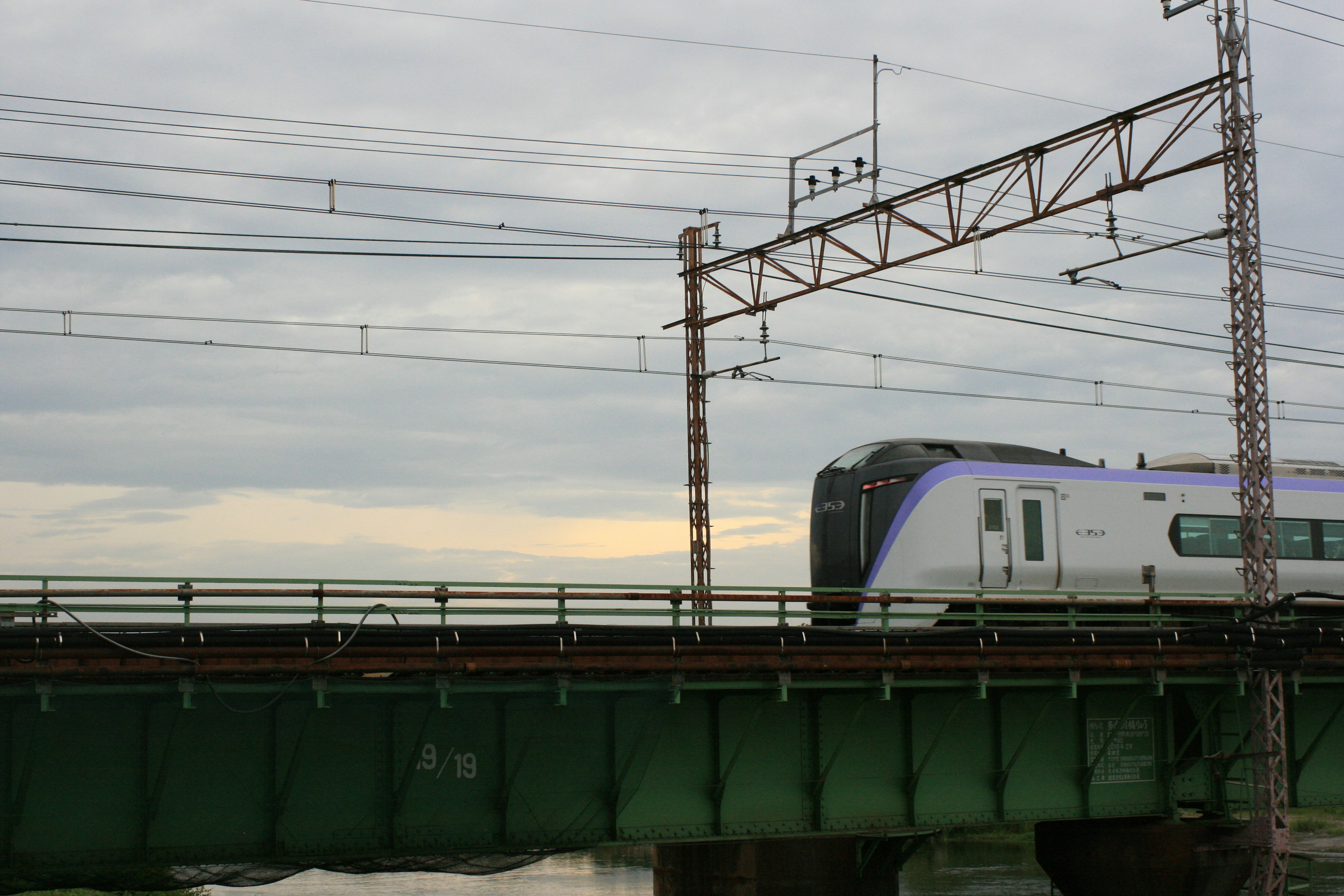 Train crossing a green bridge under a cloudy sky