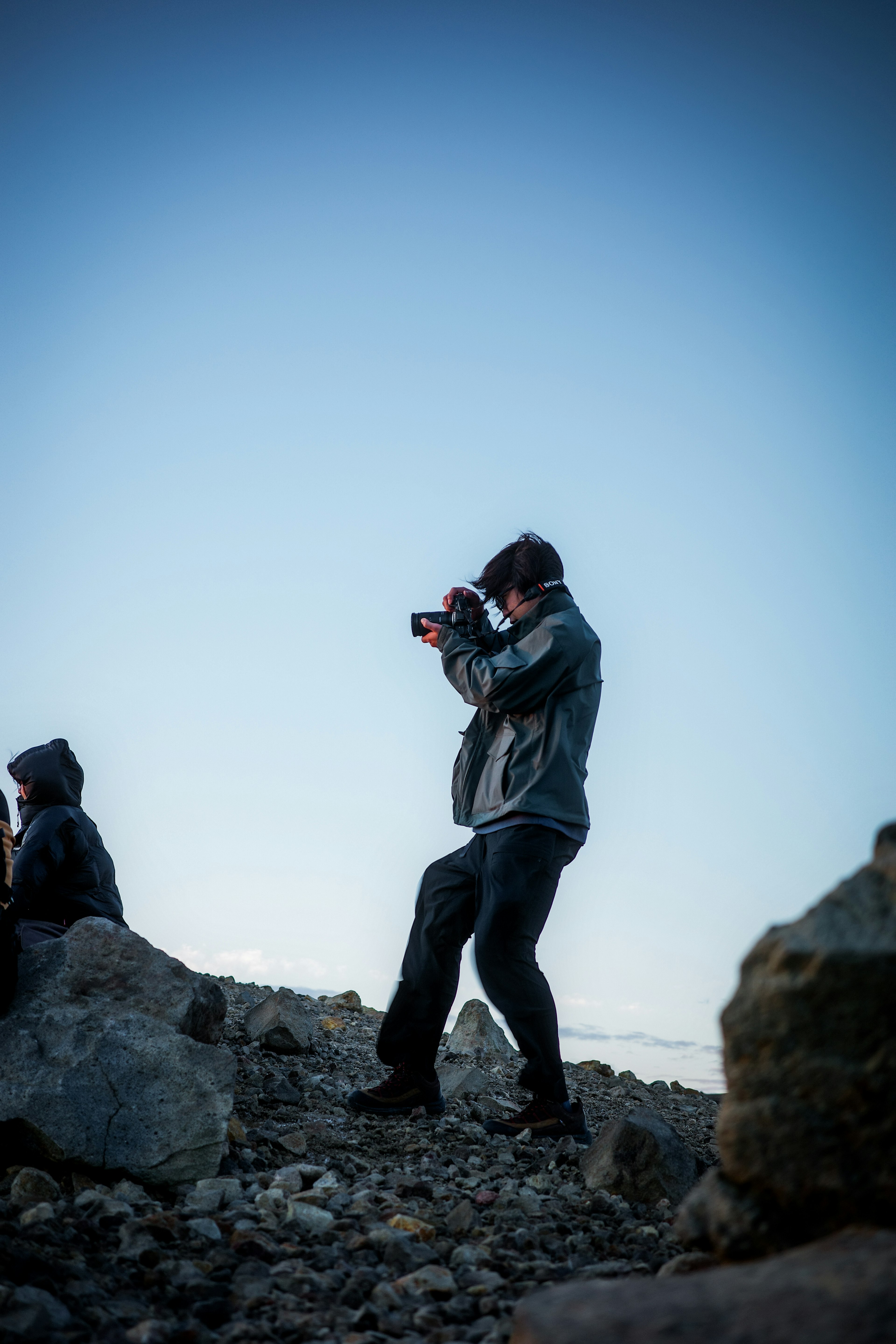 Silhouette di un uomo con una macchina fotografica su un terreno roccioso contro un cielo blu