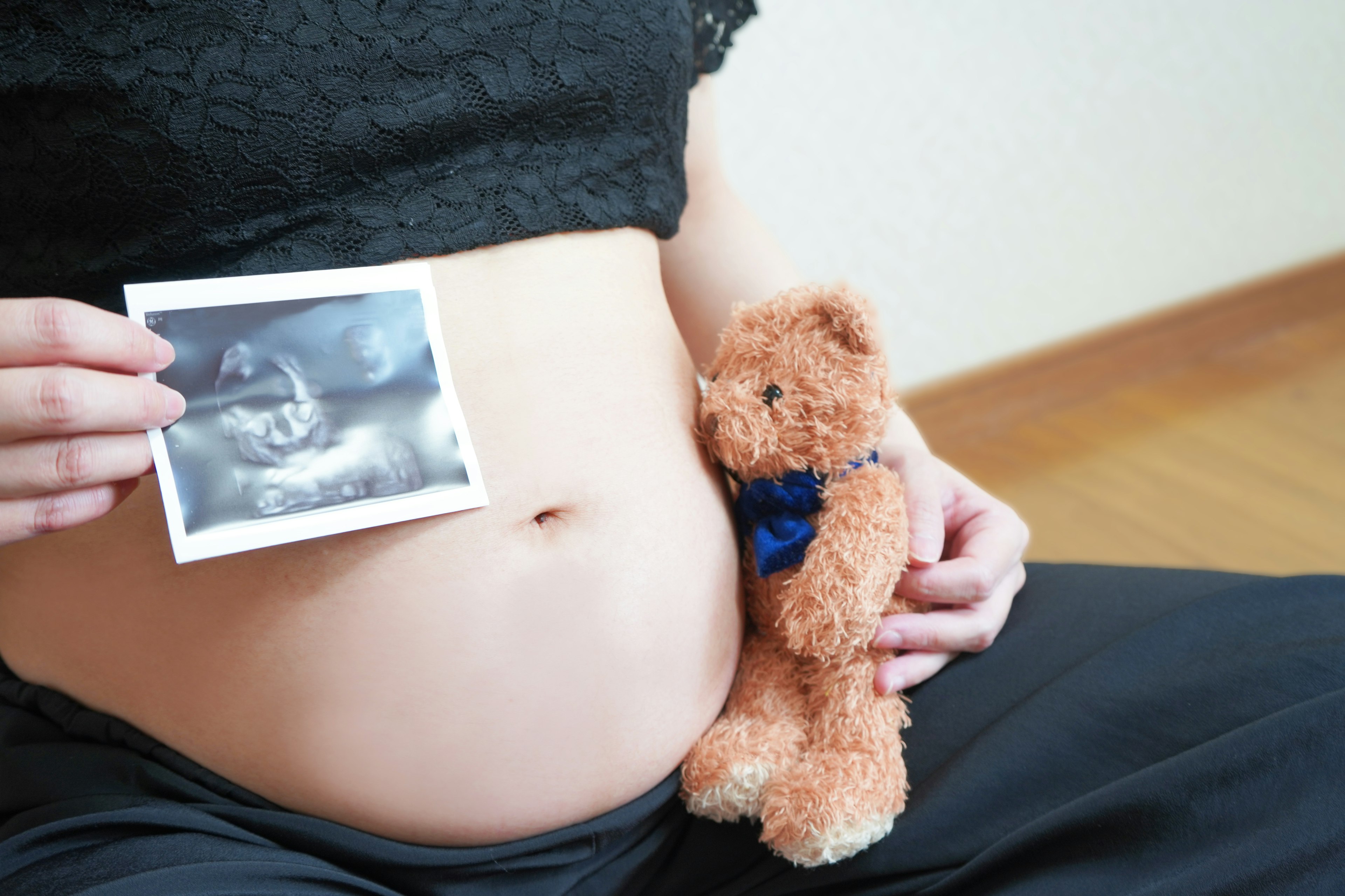 Schwangere Frau hält Ultraschallbild auf dem Bauch mit einem Teddybär