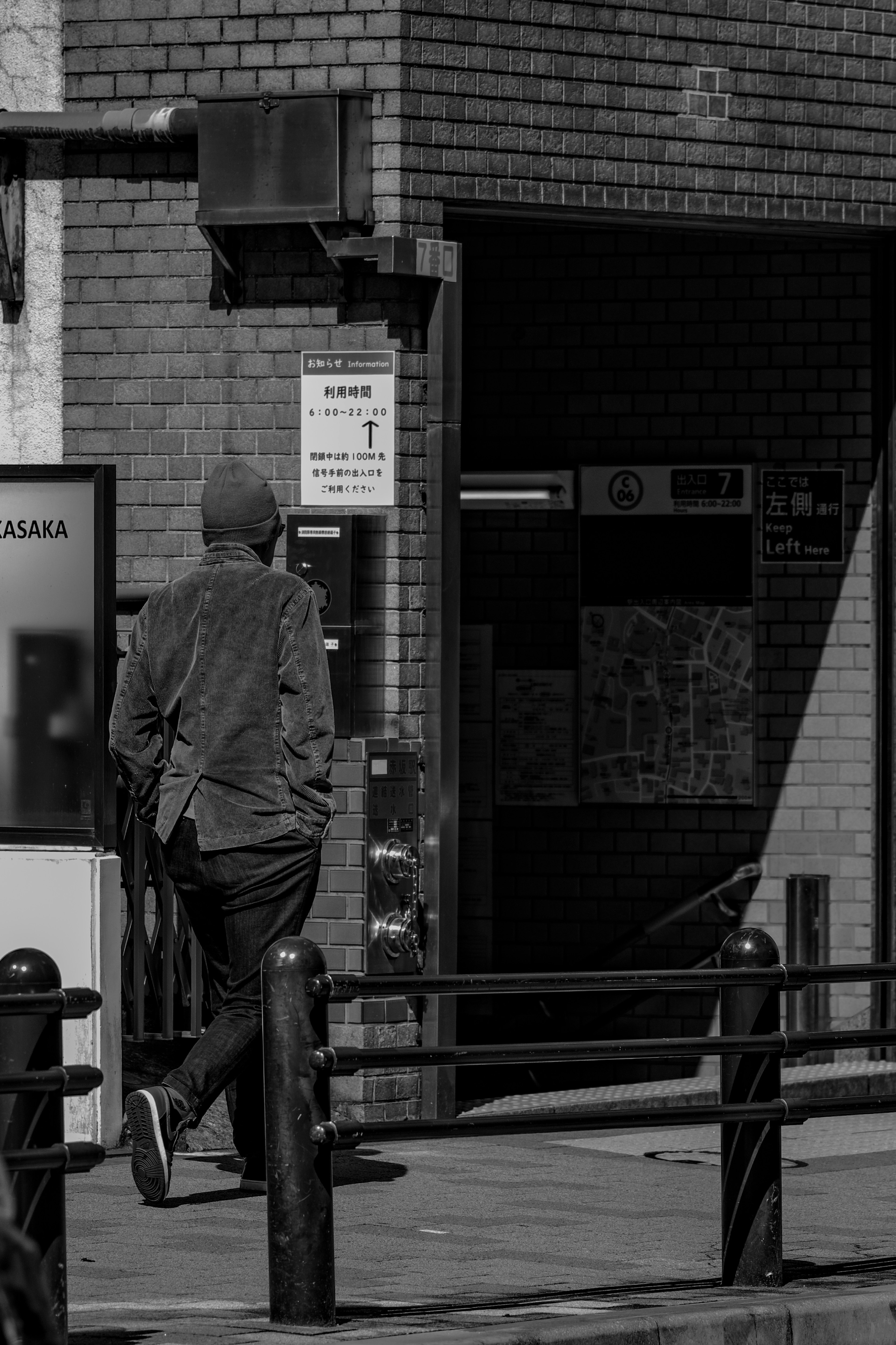 Scena di strada in bianco e nero con un uomo in cappello che cammina verso un edificio