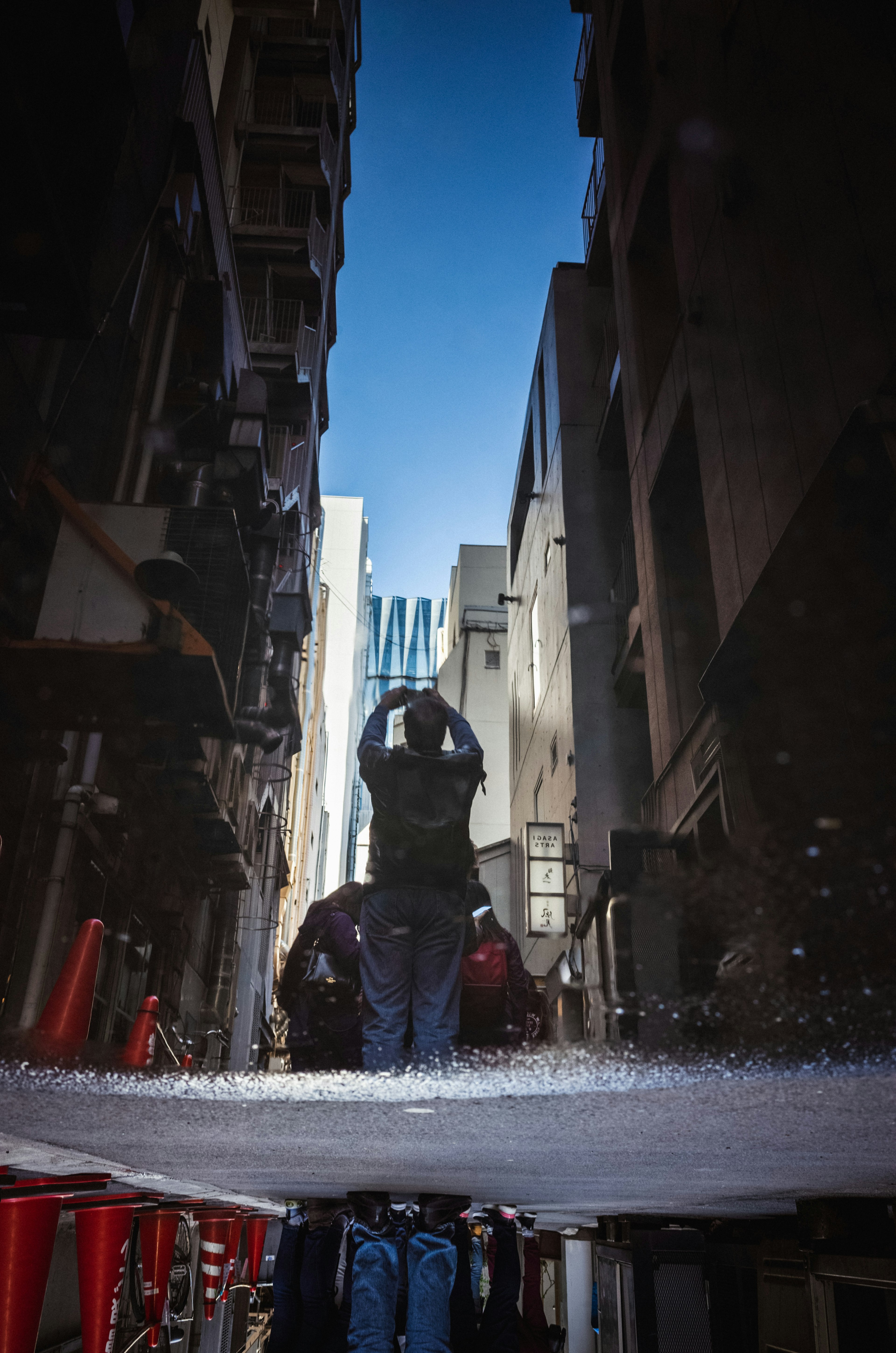 Worker spraying water in a narrow alley with buildings on either side