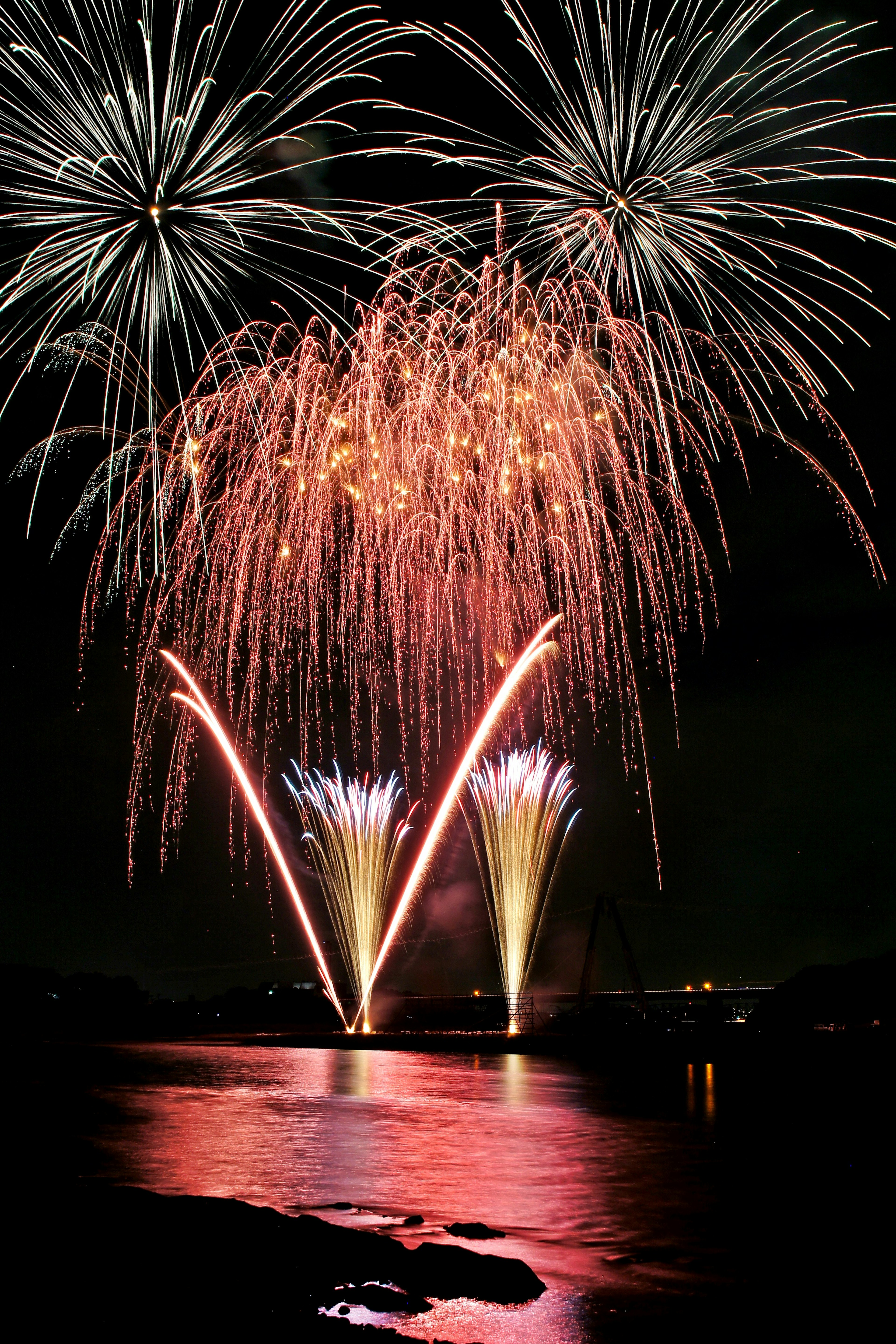 Fuegos artificiales coloridos estallando en el cielo nocturno reflejándose en el agua