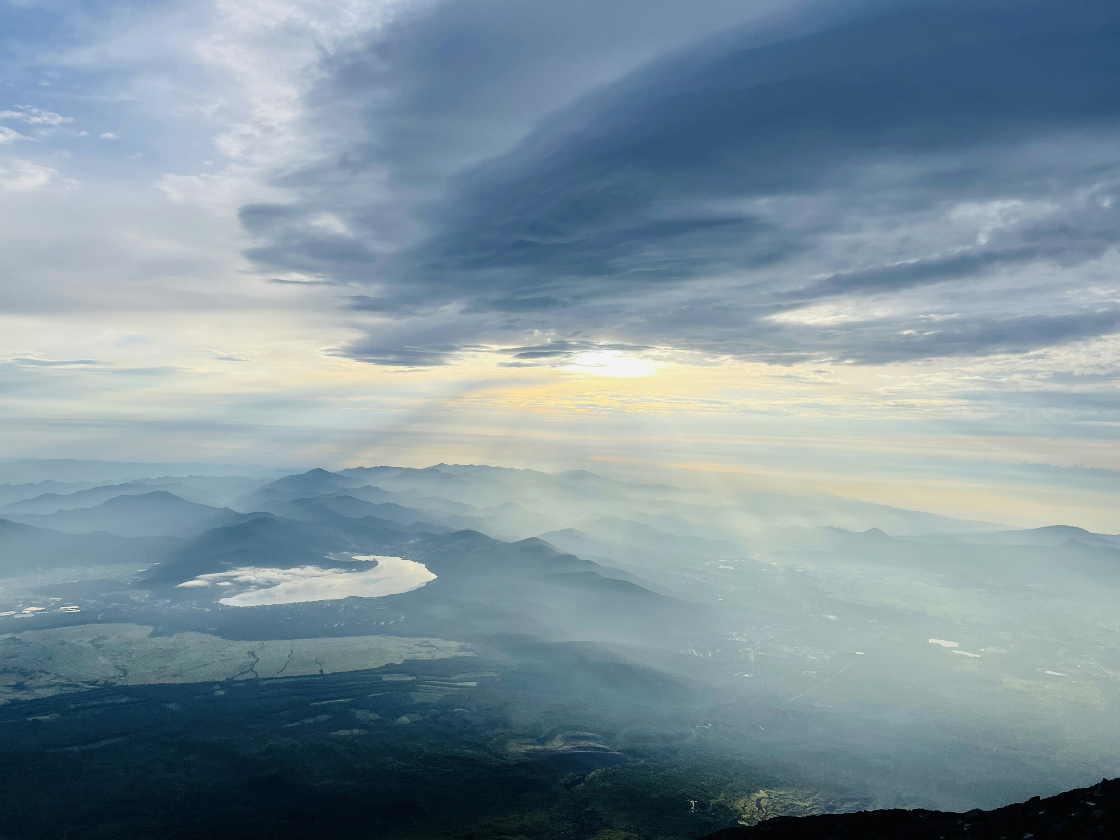 Vista escénica desde la cima de una montaña con nubes y rayos de luz sobre montañas distantes y un lago