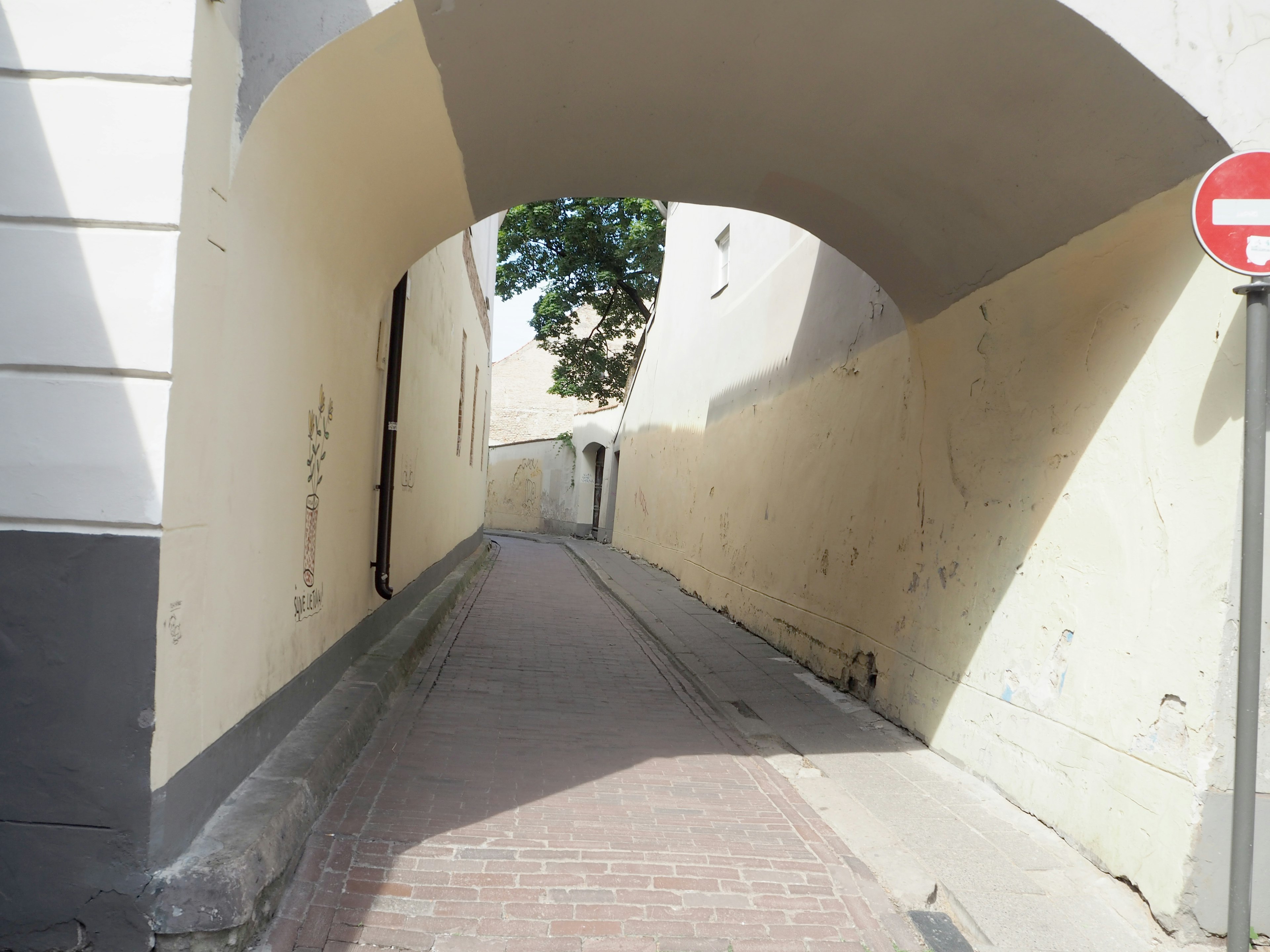 Pasaje estrecho en arco que conduce a un camino iluminado por el sol con paredes de color crema y edificios blancos a cada lado