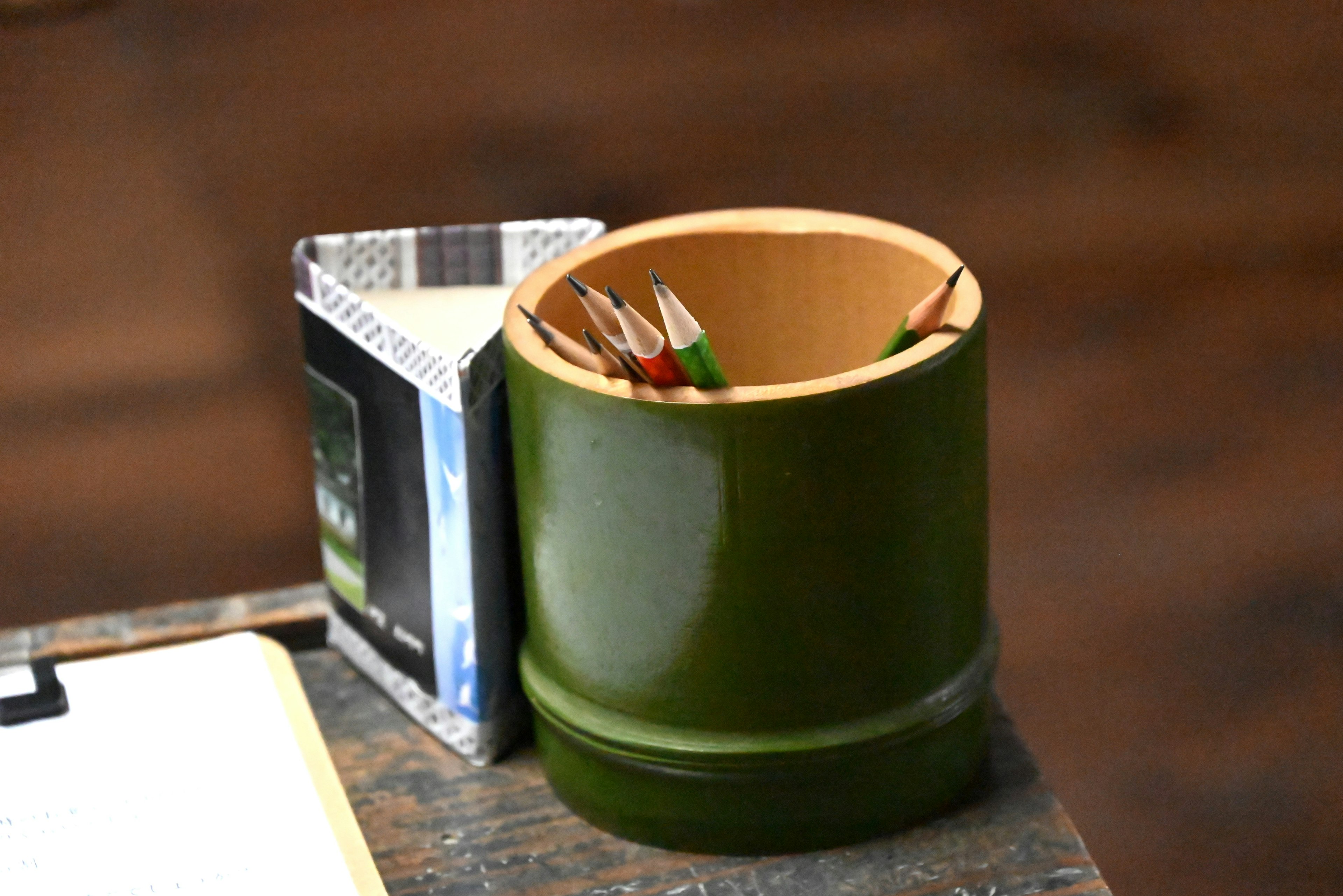 Green bamboo pencil holder with colored pencils and a square box on a desk