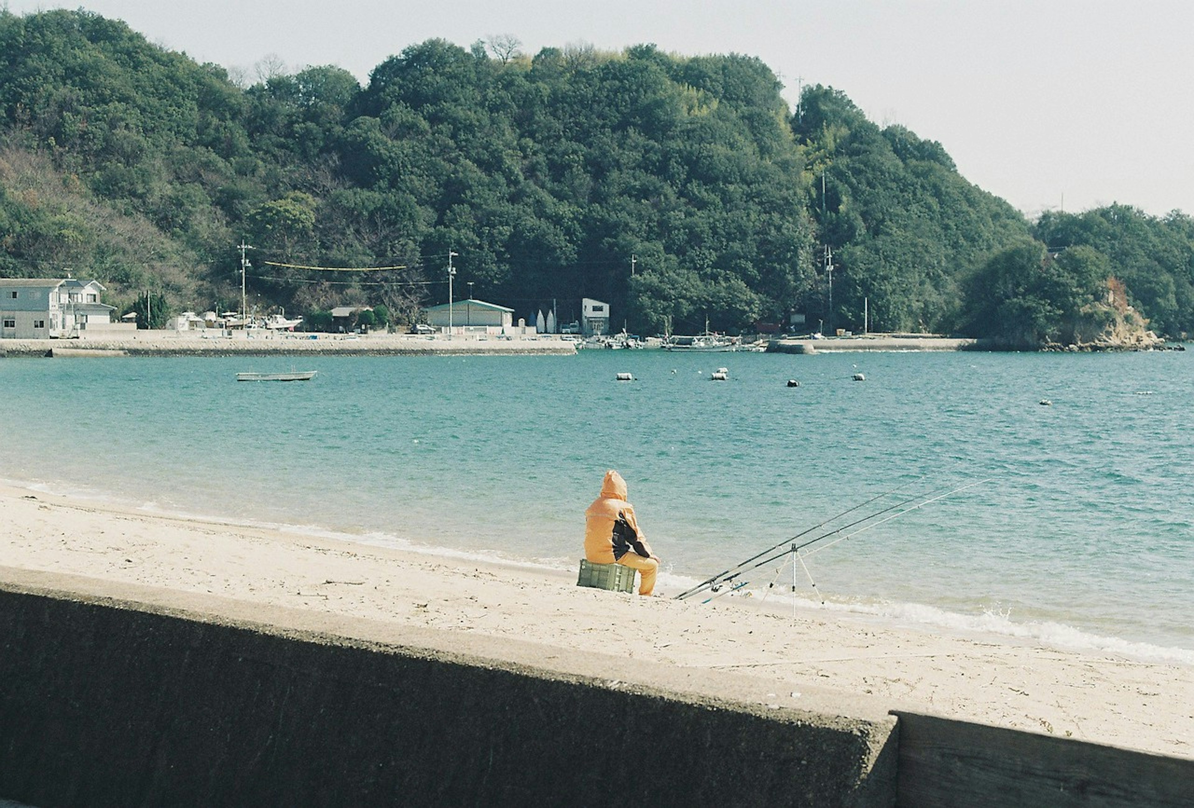 海辺で釣りをする黄色いレインコートの人物と静かな風景