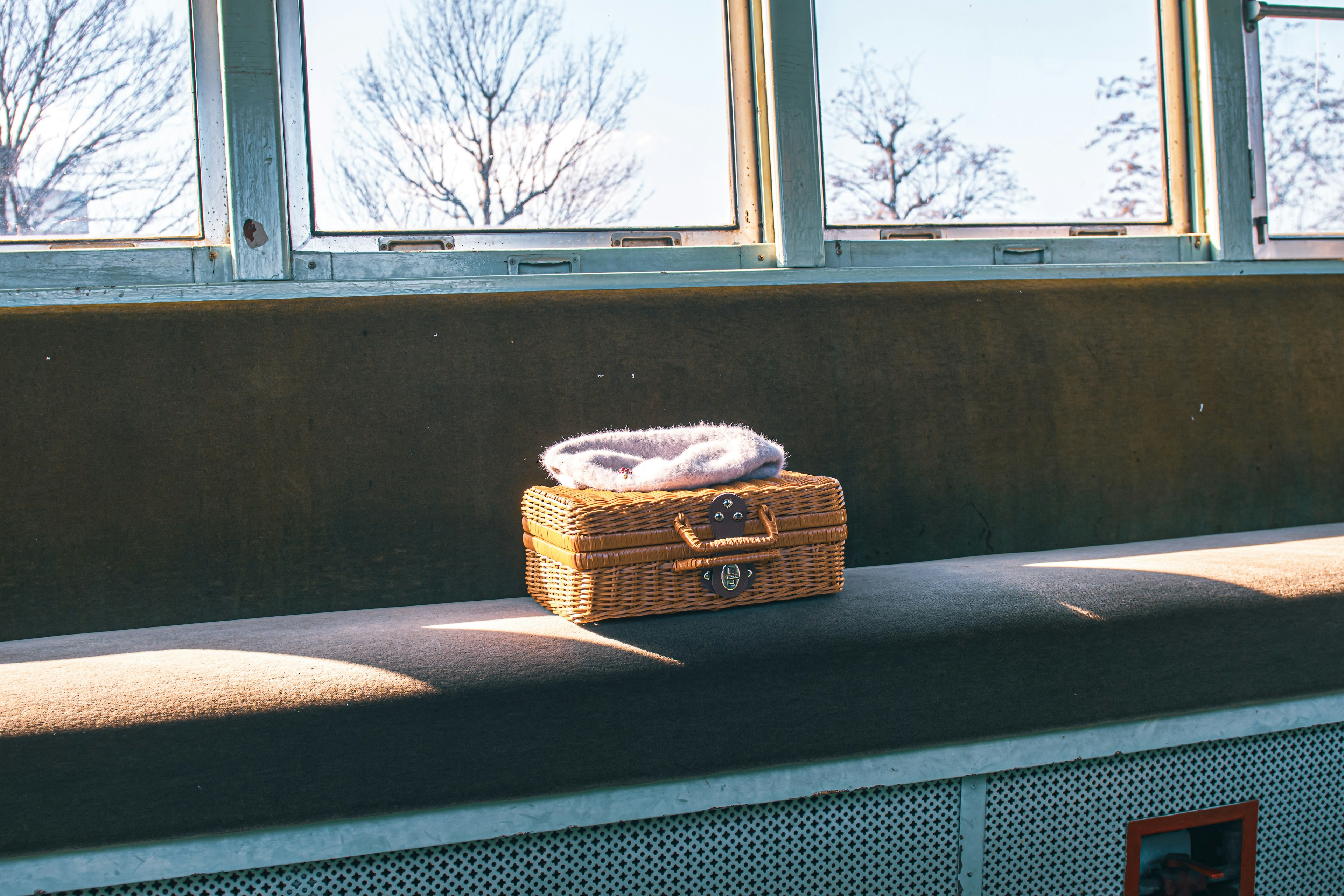 A wicker basket with a blanket on top placed by the window