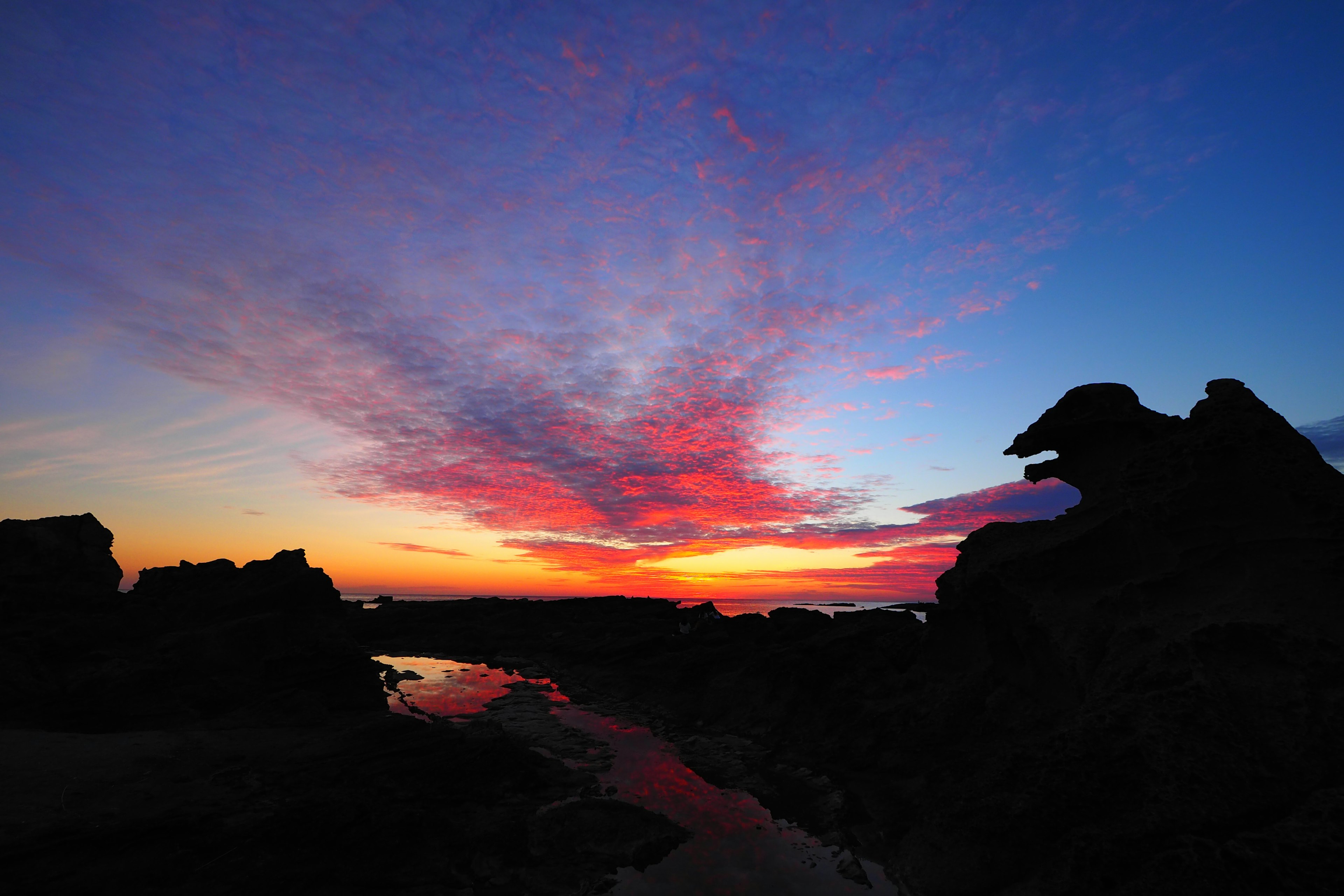 ทิวทัศน์ชายฝั่งที่น่าทึ่งพร้อมสีสันของพระอาทิตย์ตกและเงาของหิน