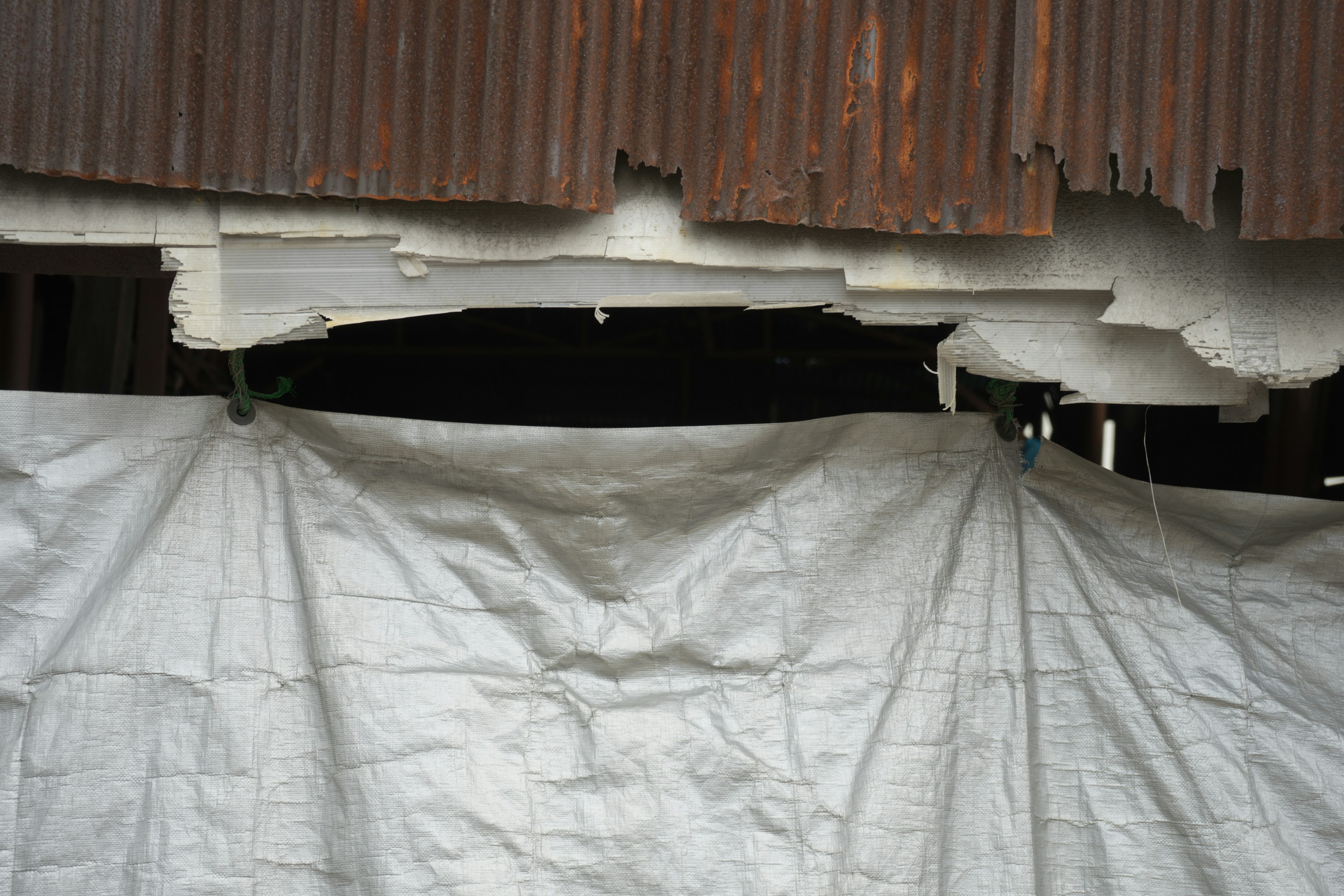 Damaged wall revealing a dark interior with a white tarp