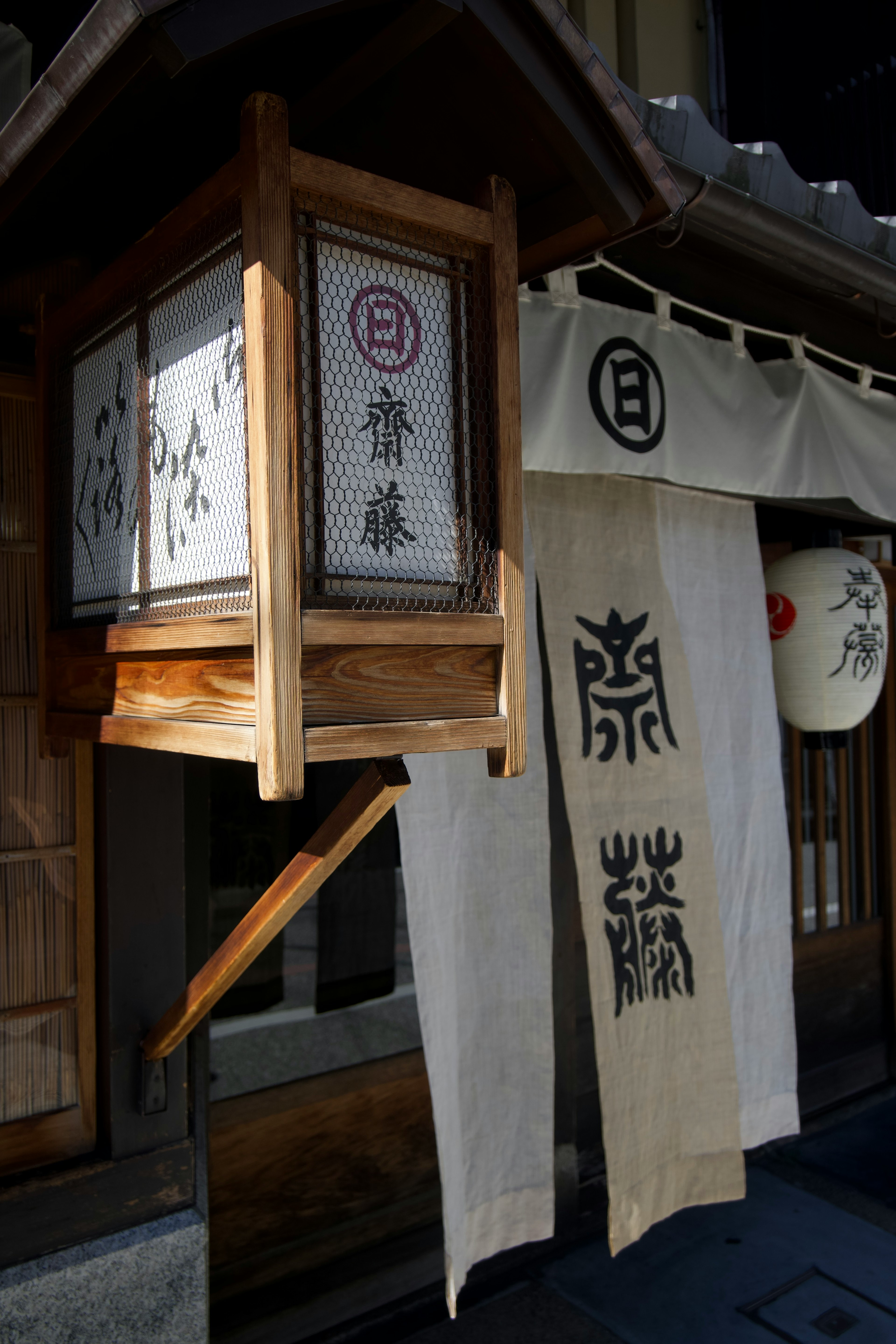 Exterior de una tienda japonesa tradicional con una linterna de madera y un noren de tela