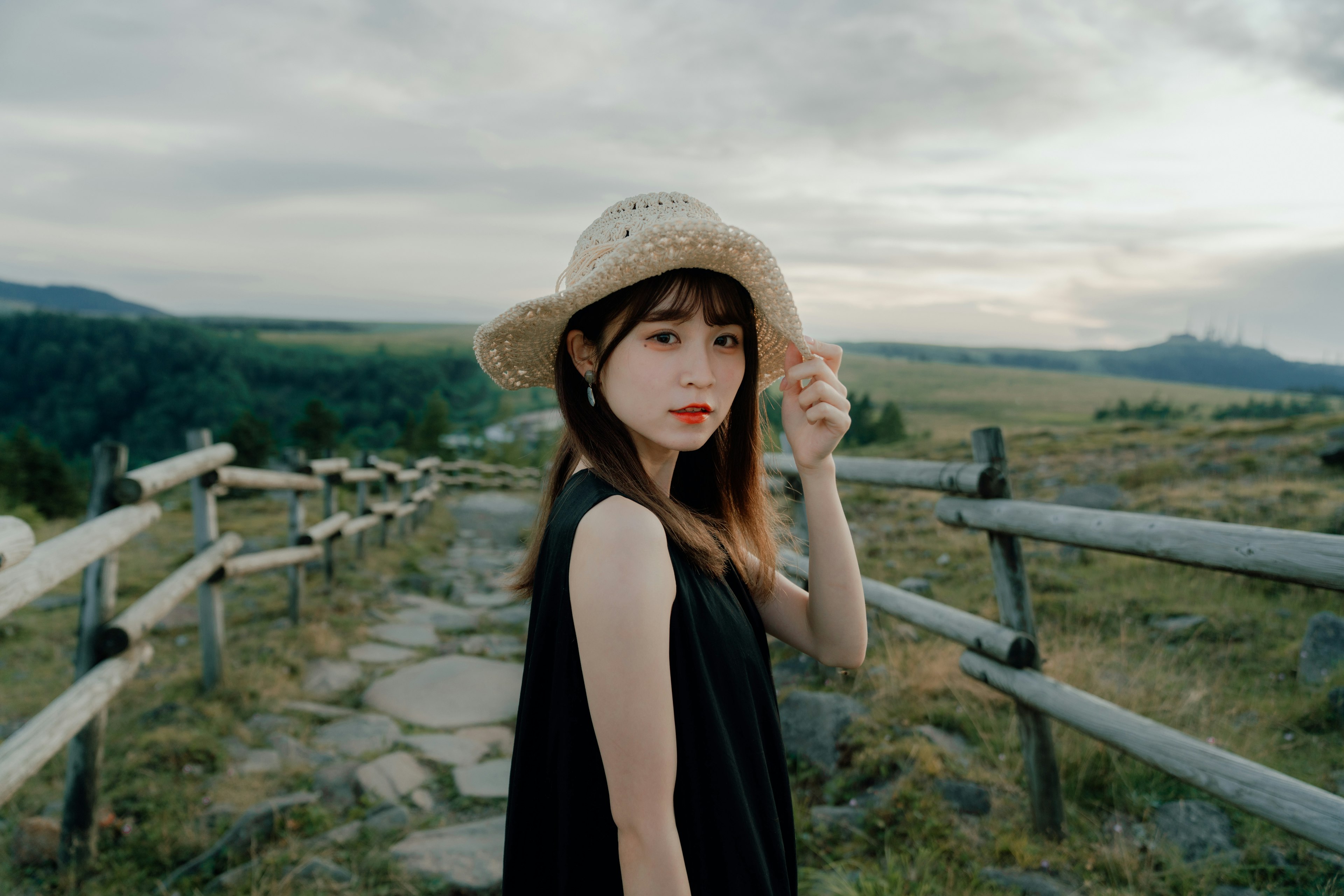 A woman wearing a straw hat standing against a scenic landscape