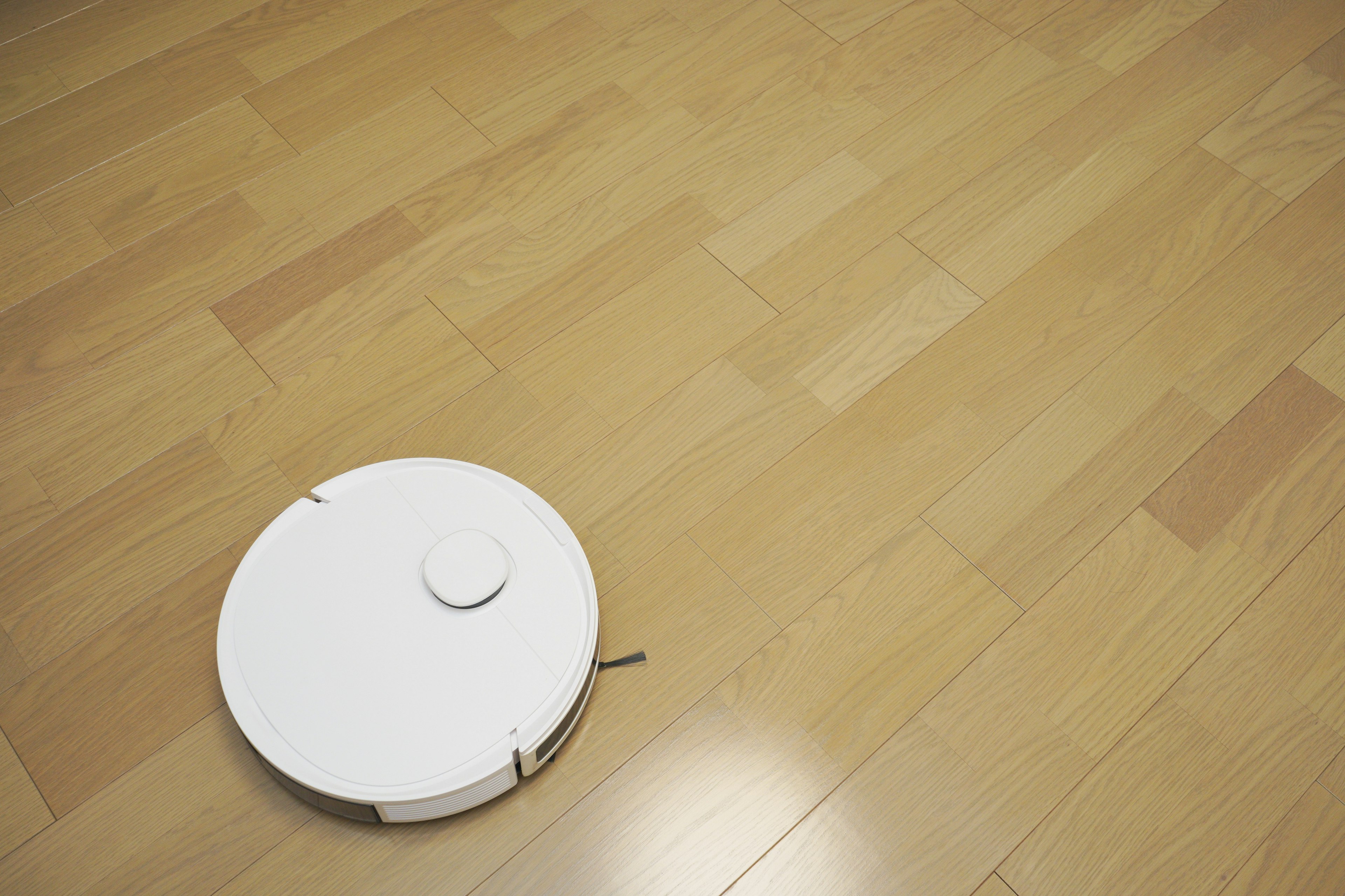 White robotic vacuum cleaner on a light wooden floor