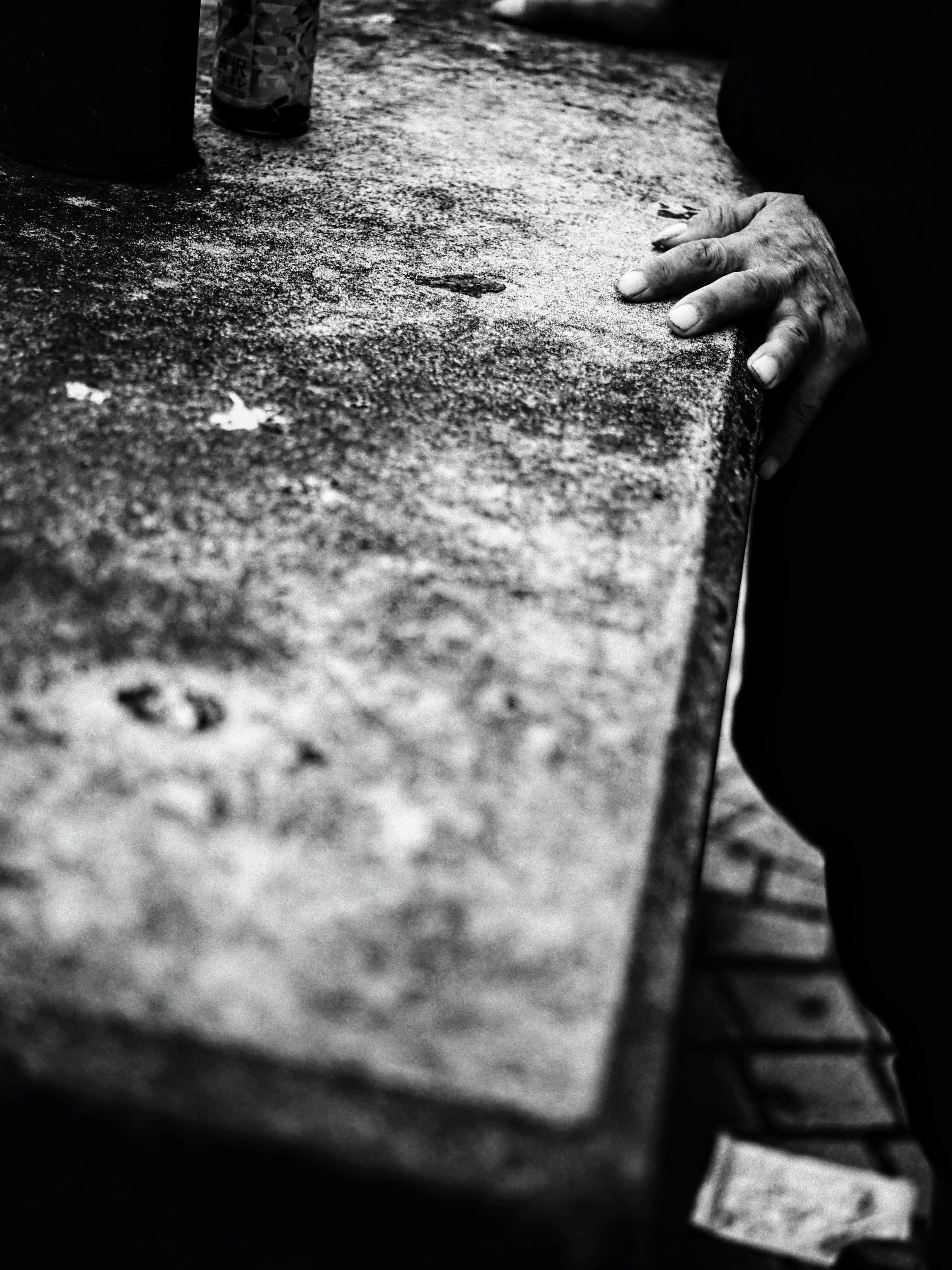 Immagine in bianco e nero di una mano appoggiata su un vecchio tavolo in cemento