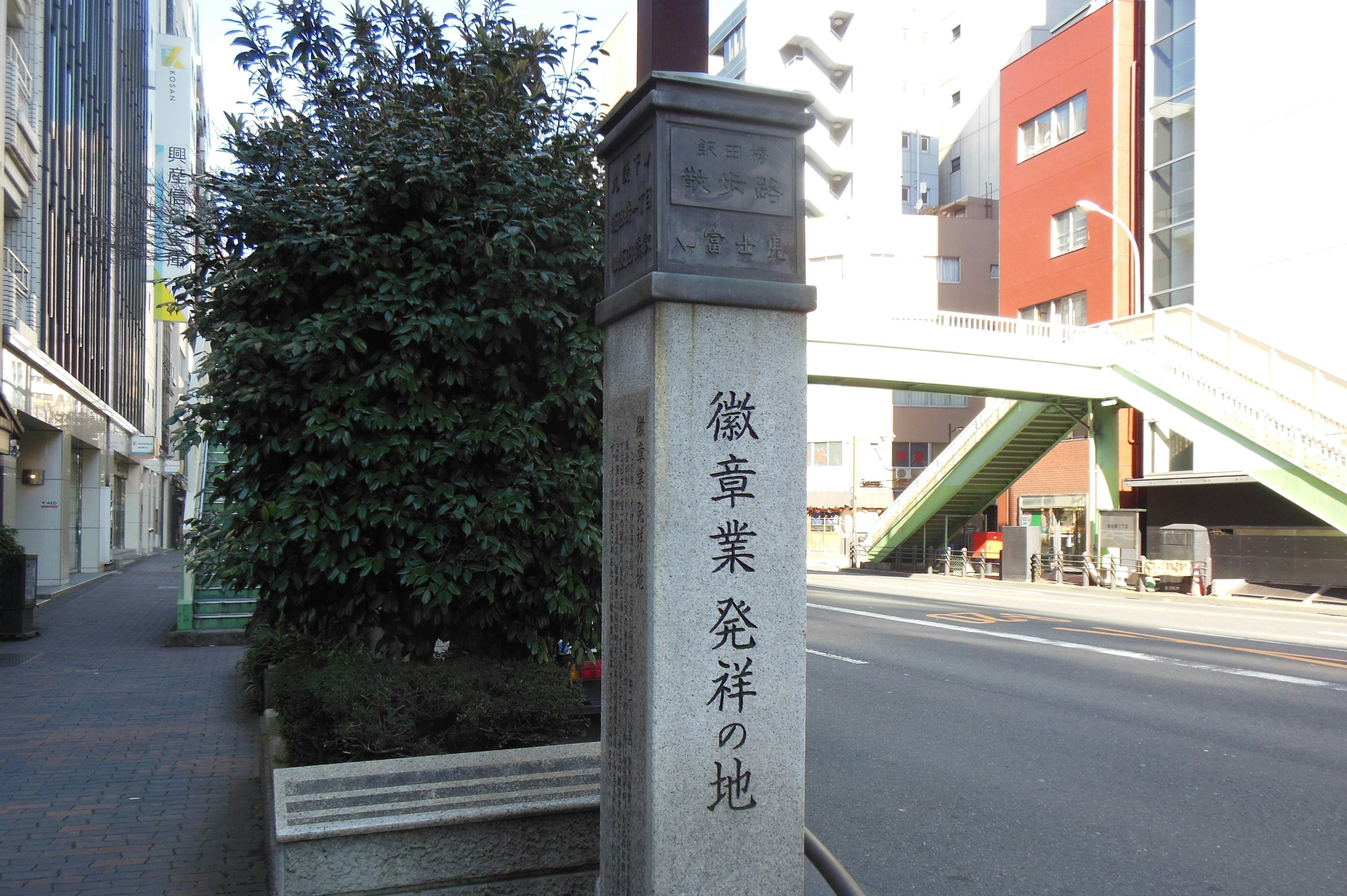 Stone signpost at a street corner with greenery and buildings nearby