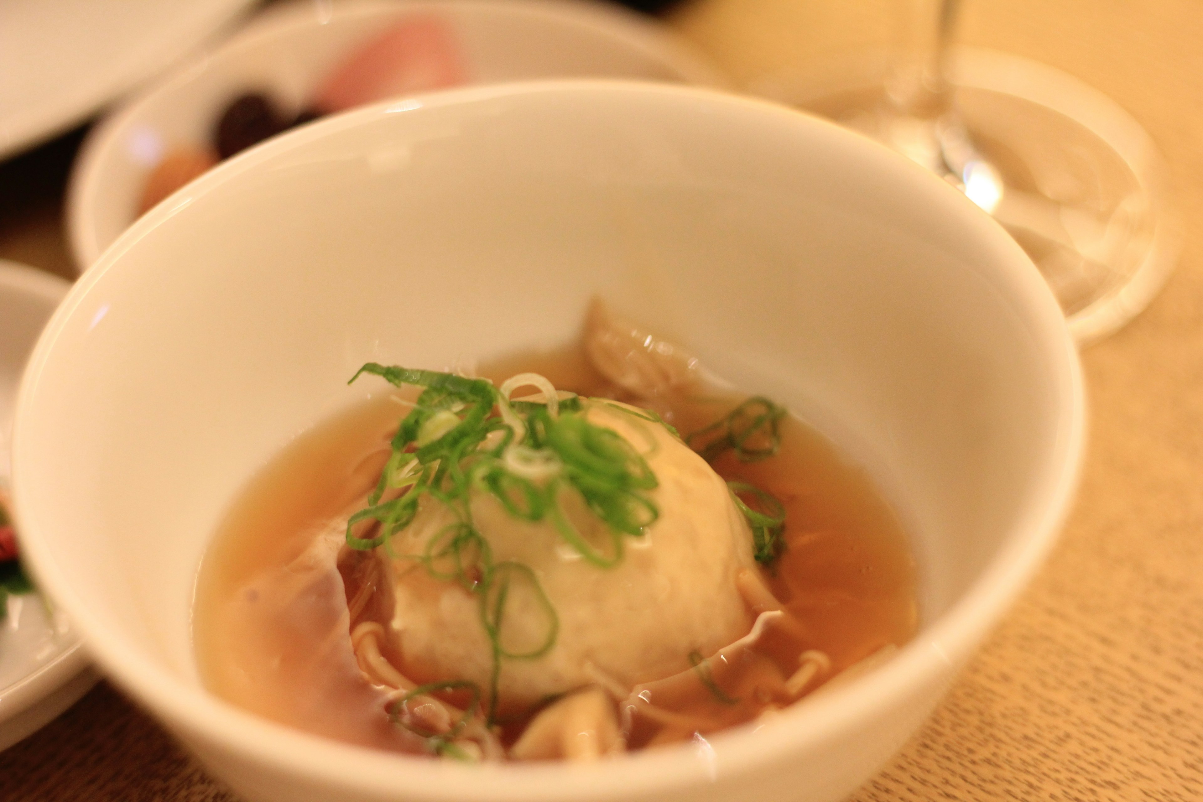 A bowl of meatball in broth garnished with green onions