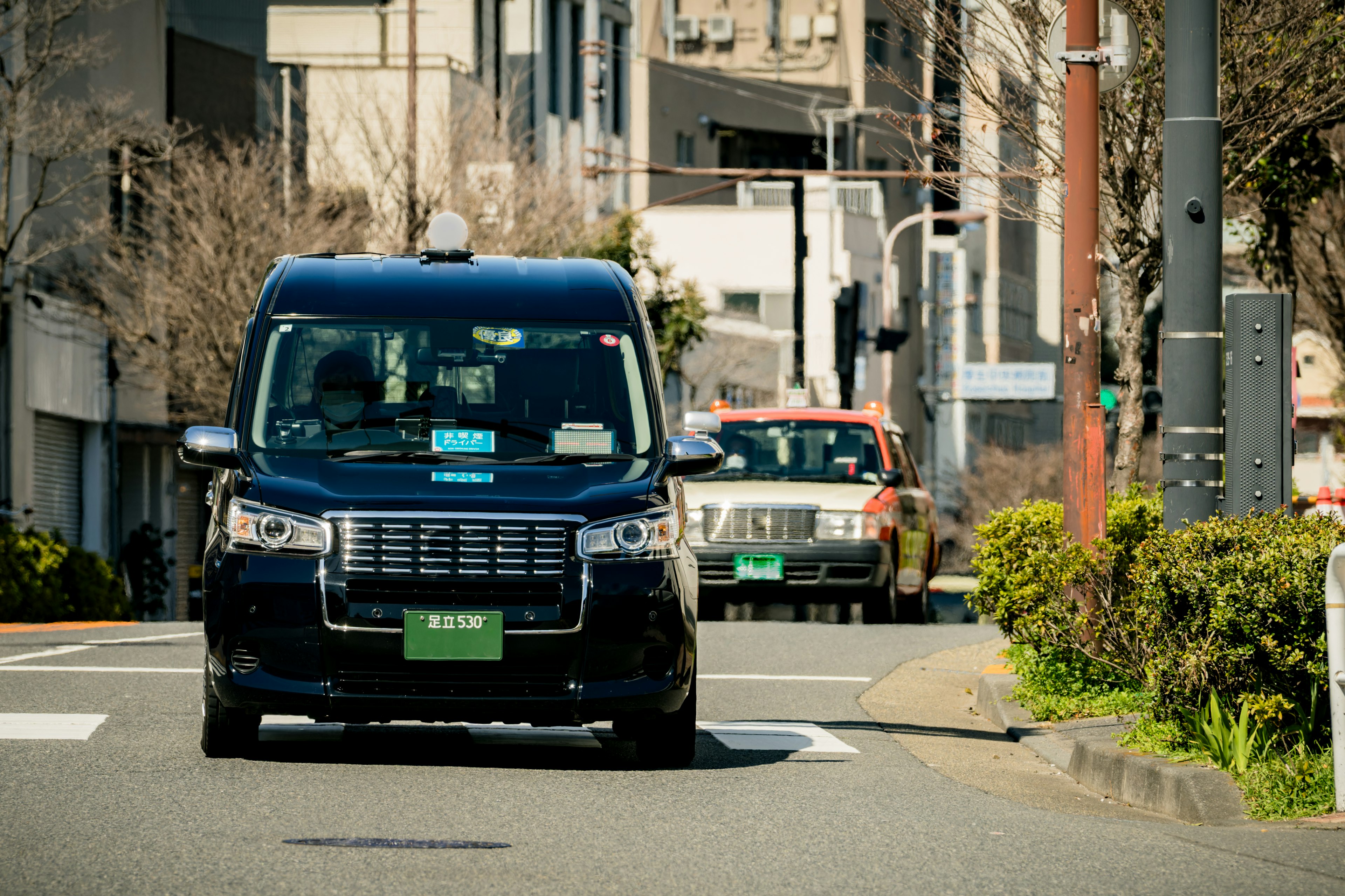 A black taxi driving on a street with buildings in the background