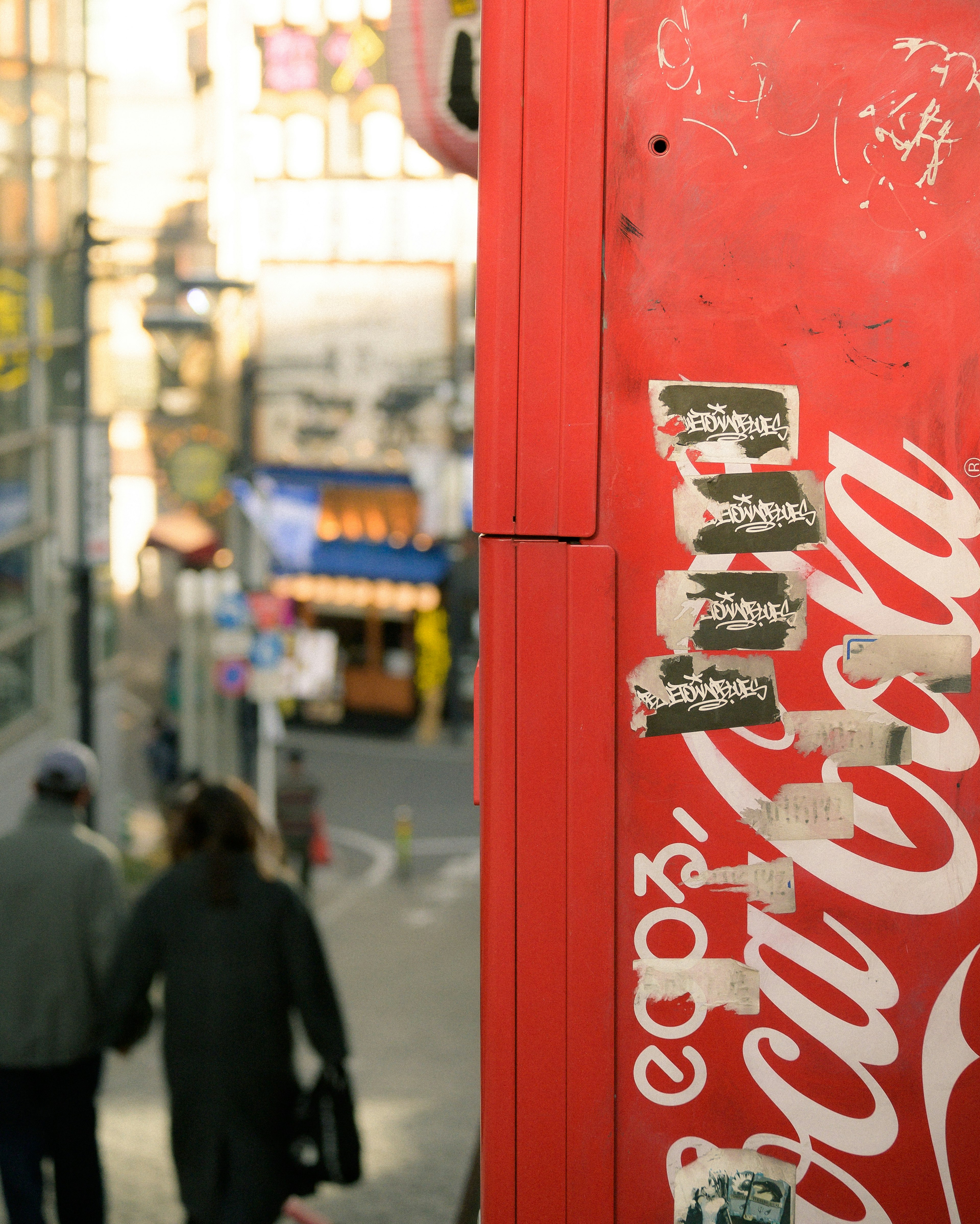 Máquina expendedora Coca-Cola roja con una pareja caminando por la calle