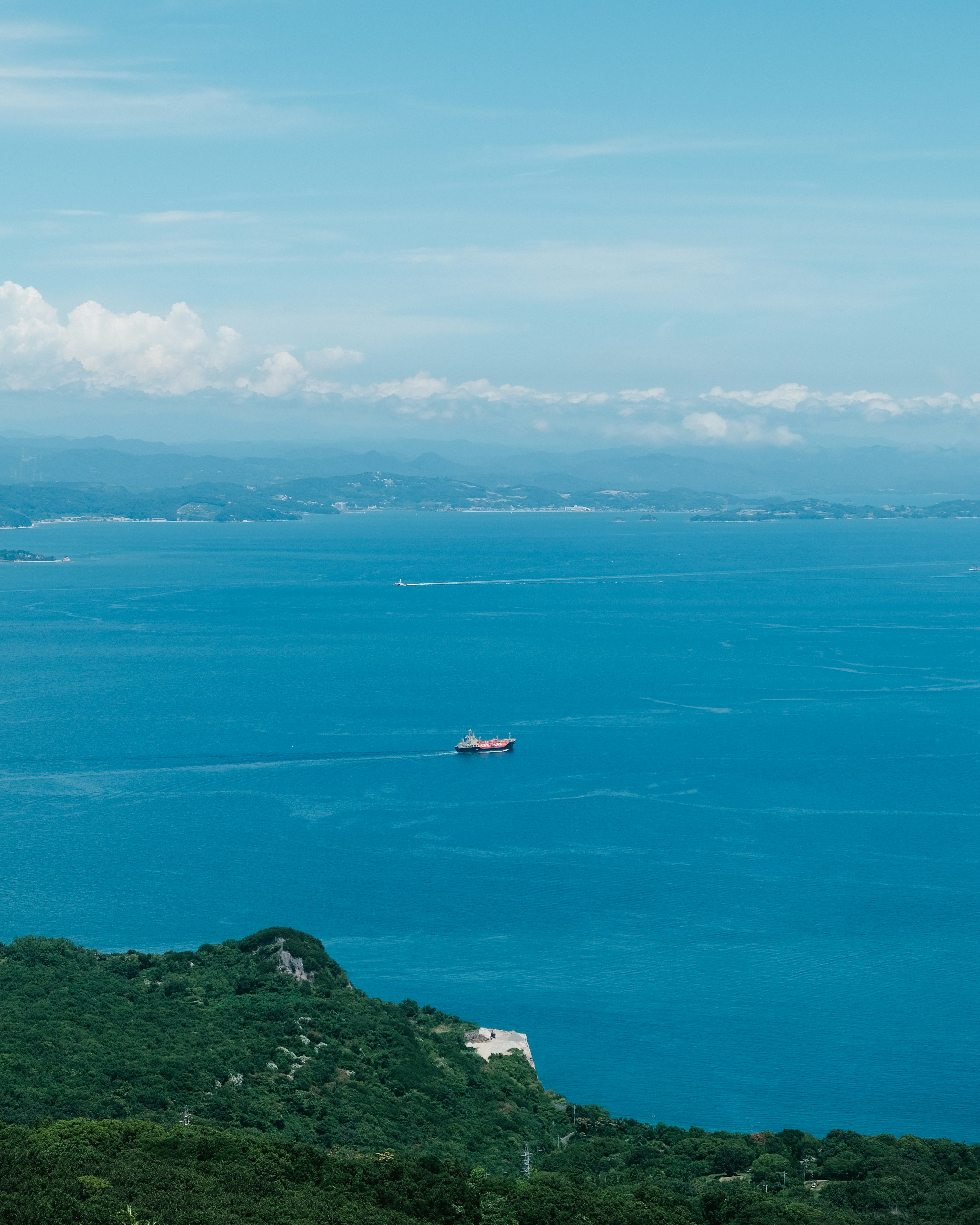 Vista escénica del océano azul con un barco colinas verdes en primer plano islas y nubes a lo lejos