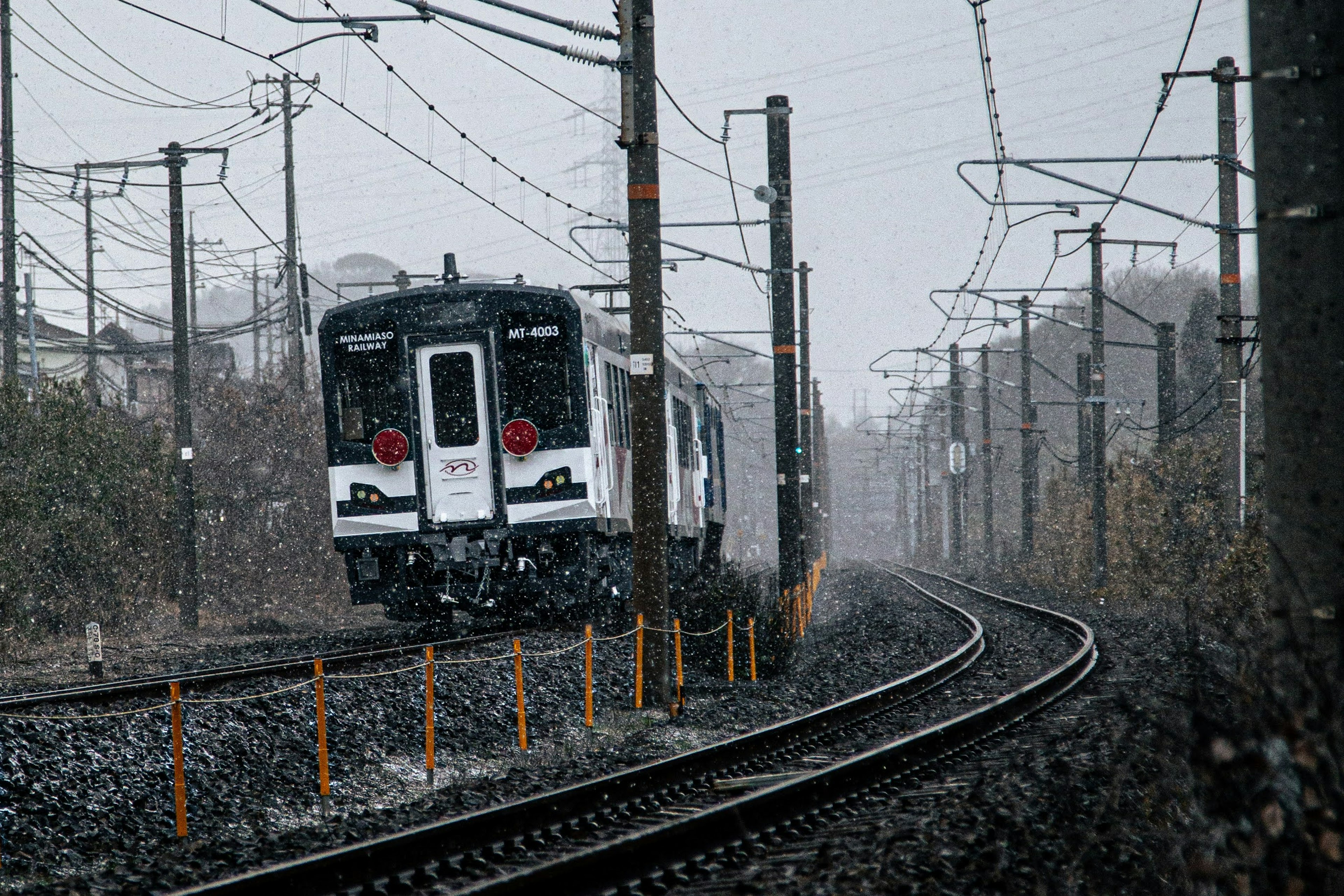 Un treno bianco e nero che viaggia nella neve con binari e pali elettrici visibili