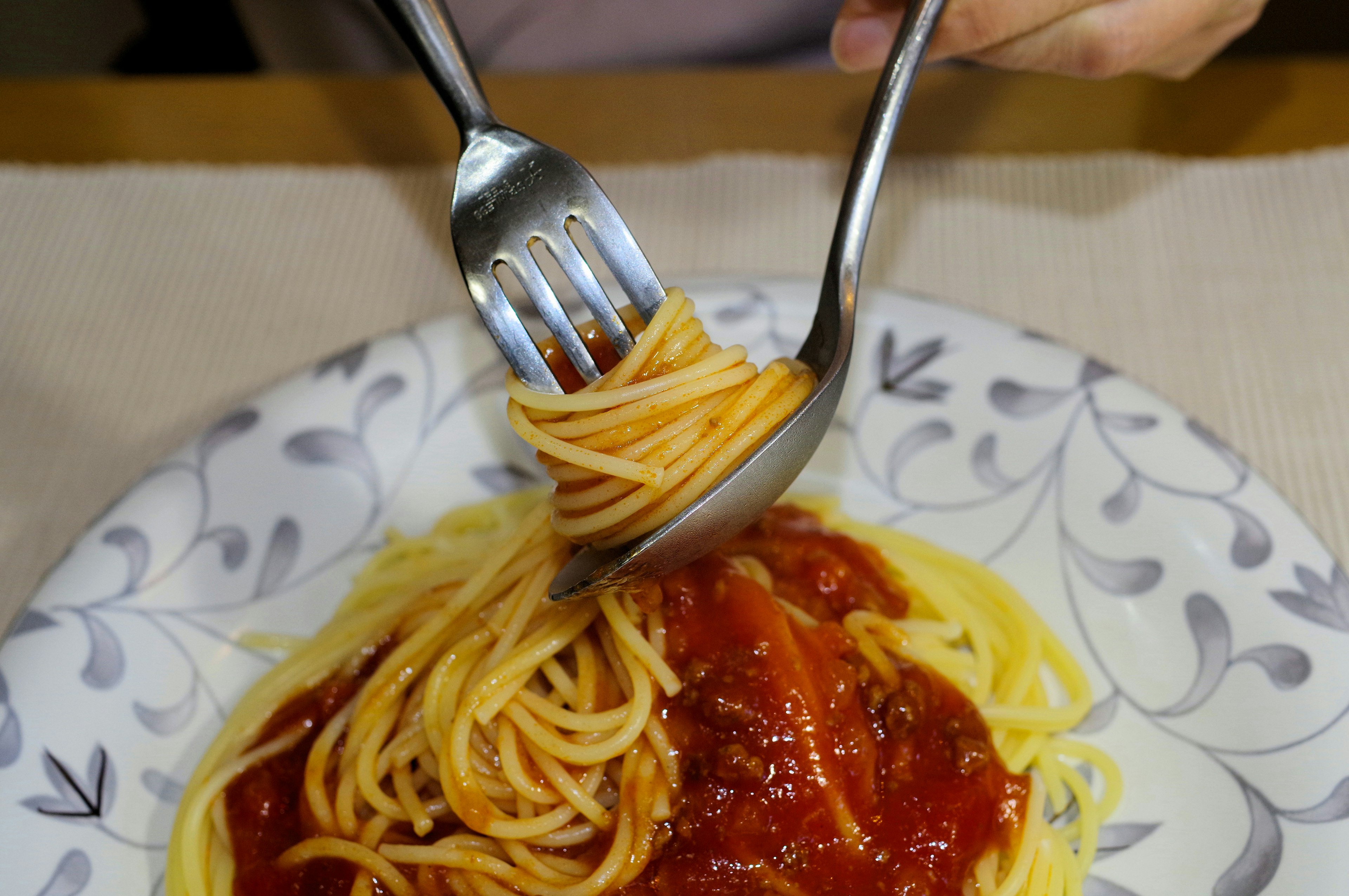 Sepiring spaghetti yang diputar dengan garpu dan sendok dalam saus tomat