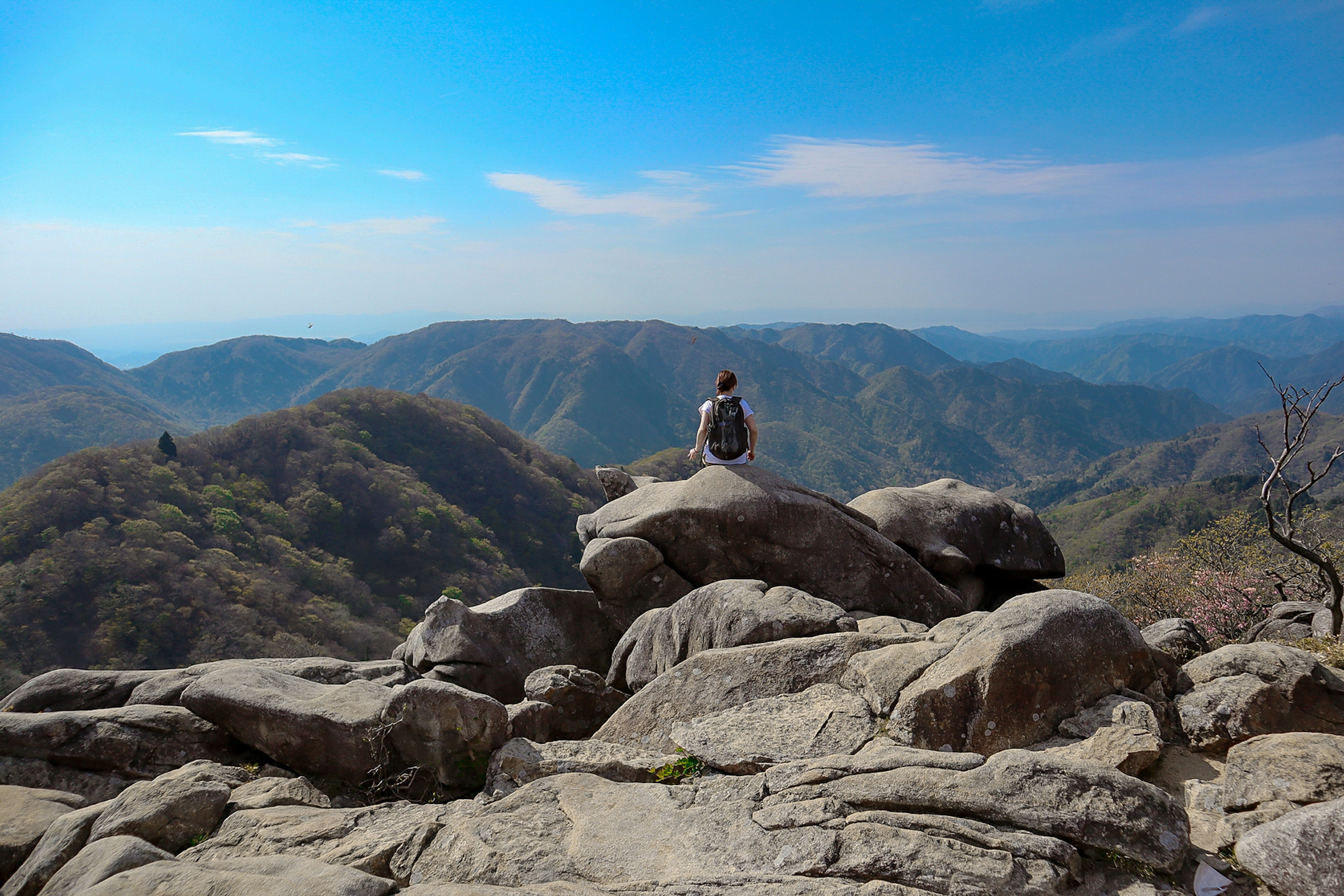 Persona sentada en la cima de una montaña rocosa con vista a un vasto paisaje