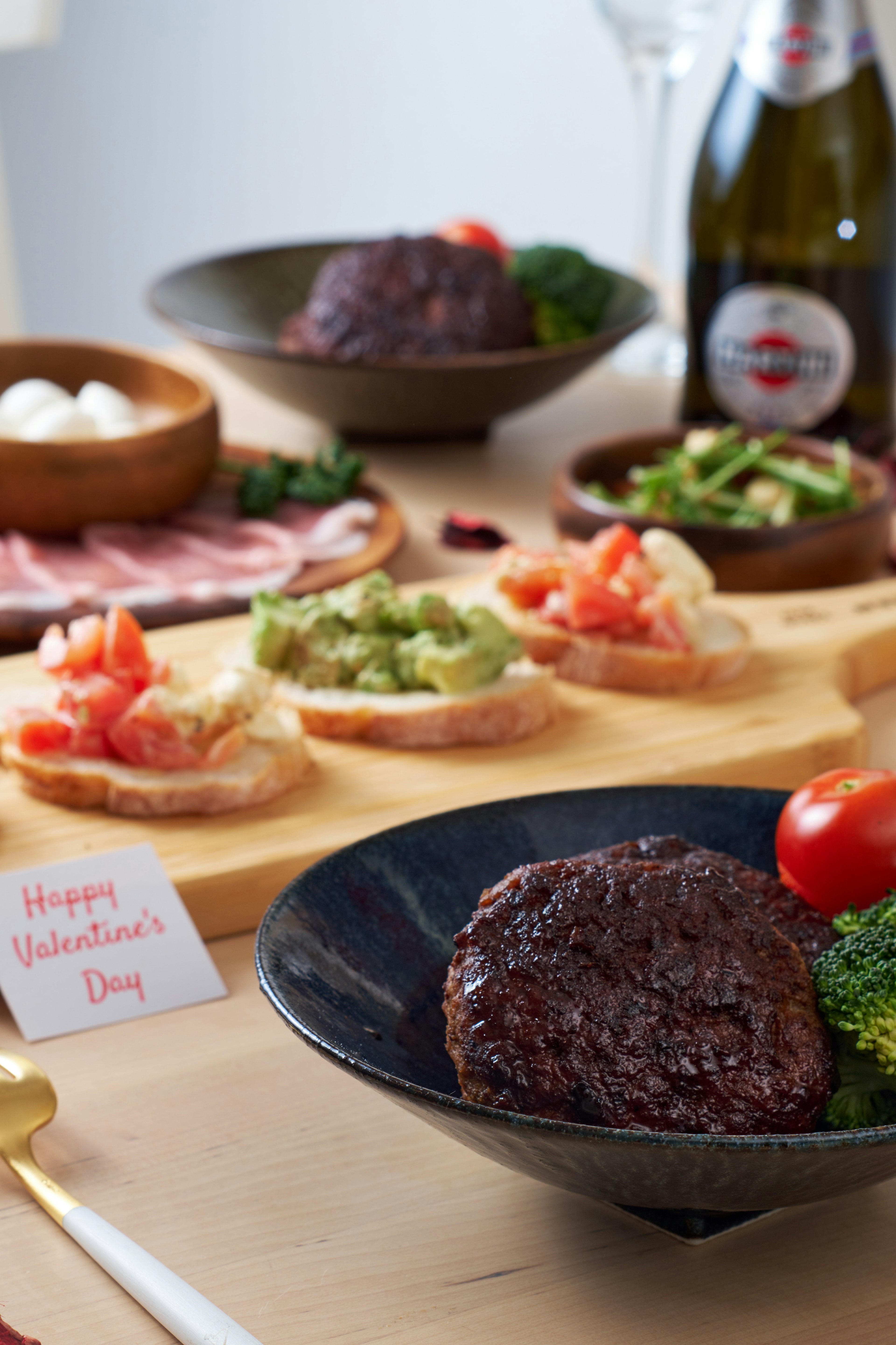 Una tavola imbandita per la cena di San Valentino con un piatto nero contenente un hamburger verdure fresche e antipasti di pane guarniti