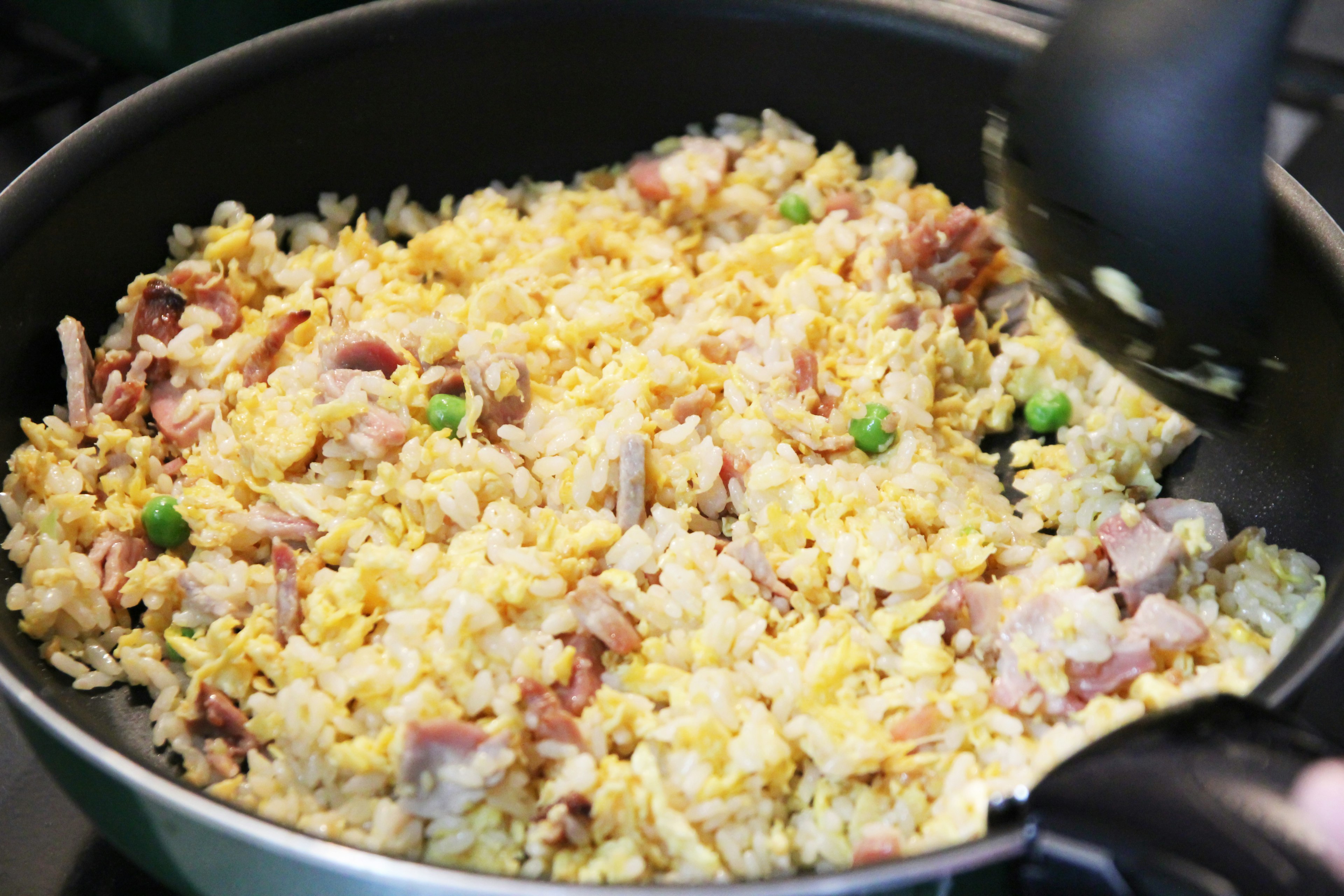 Fried rice in a pan with eggs, ham, and green peas