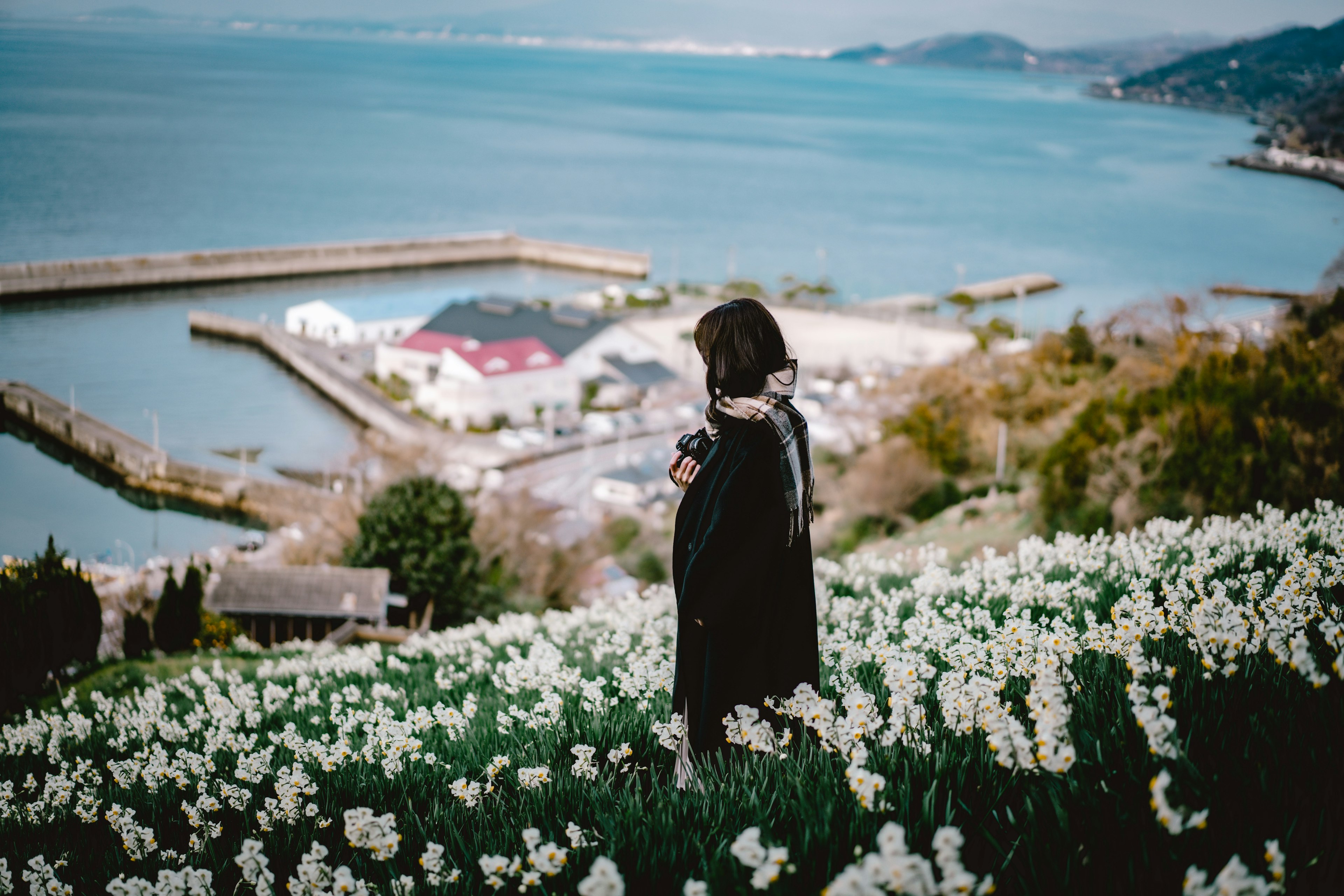 Frau steht in einem weißen Blumenfeld mit Blick auf das Meer