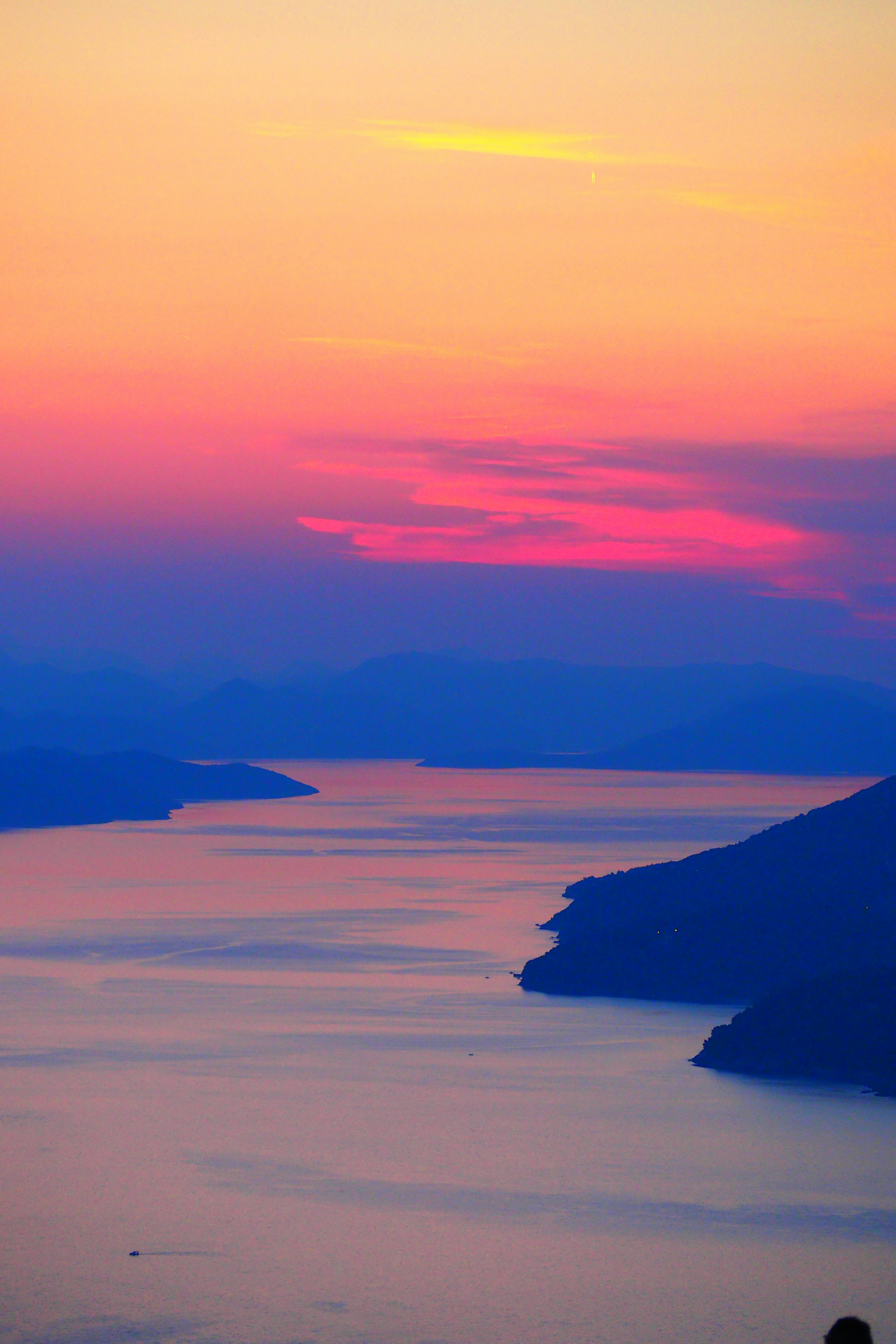 Schöne Sonnenuntergangsansicht mit Silhouetten von See und Bergen in lila und orange