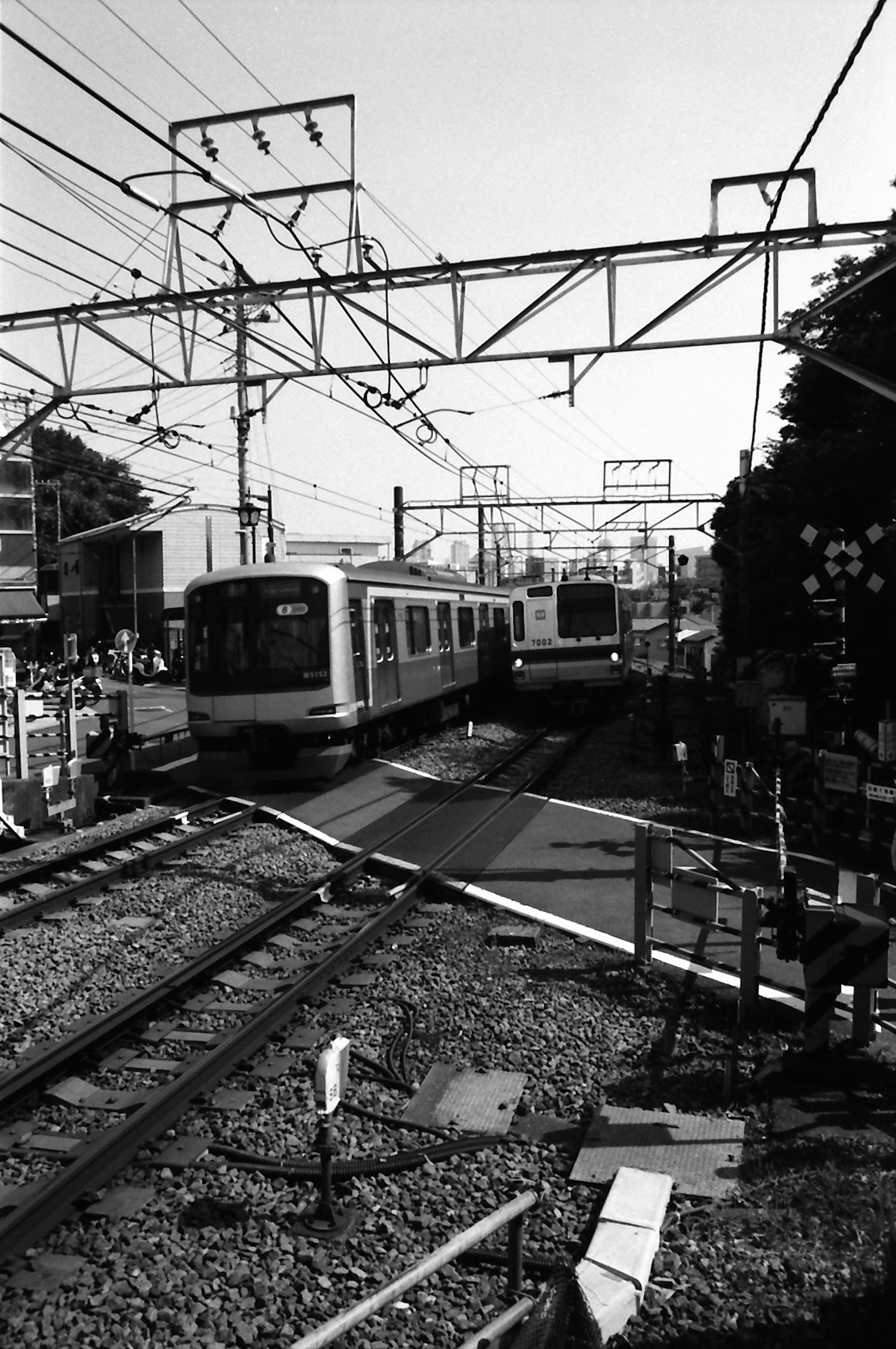 Incrocio ferroviario in bianco e nero con treni fermi e cavi aerei